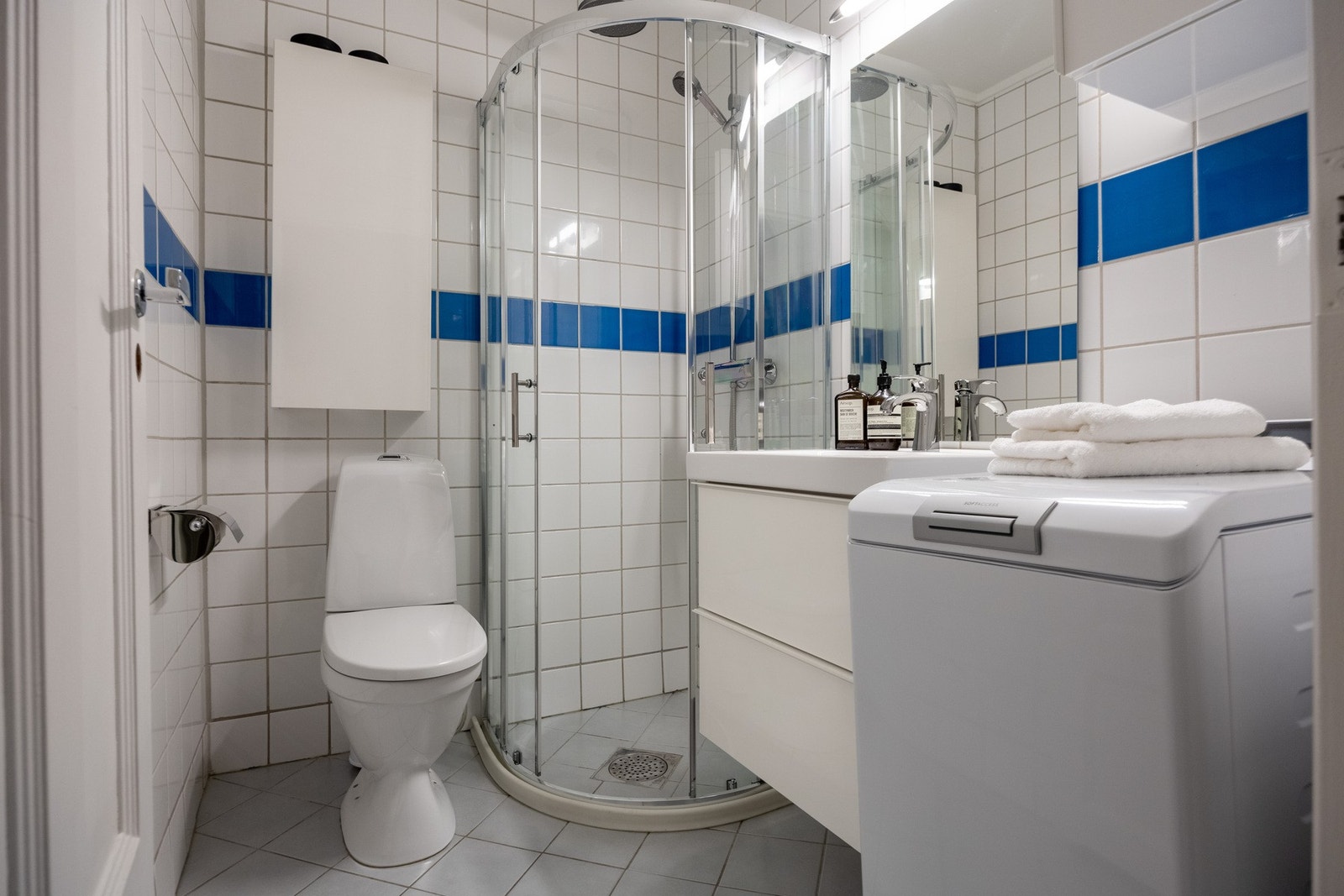 Lyst baderom med flislagt gulv med gulvvarme og opplegg for vaskemaskin. Galleribilde