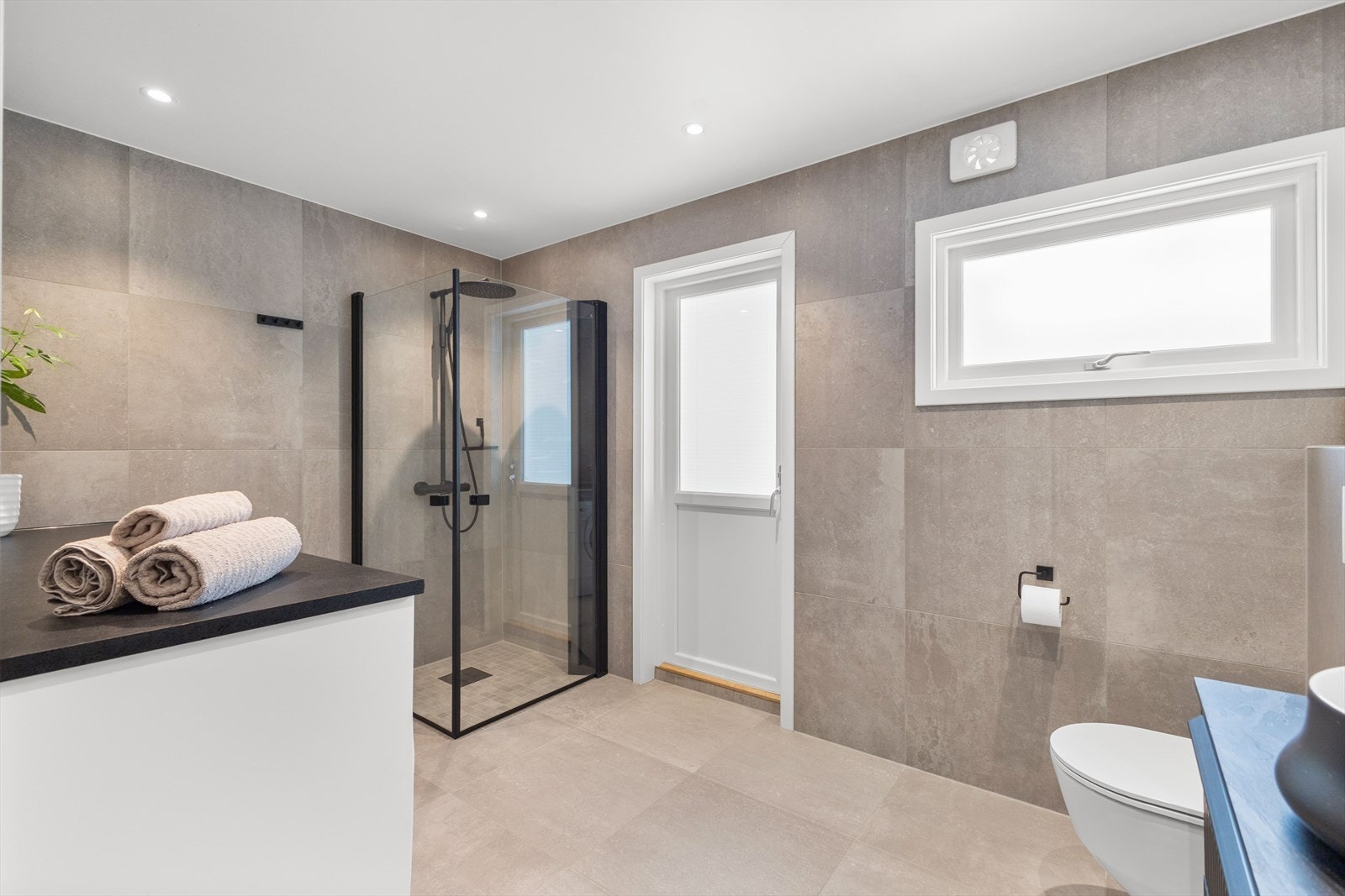 Badet er innredet med lekker servantinnredning, vegghengt toalett, dusjhjørne med glassdører og opplegg for vaskemaskin. Galleribilde