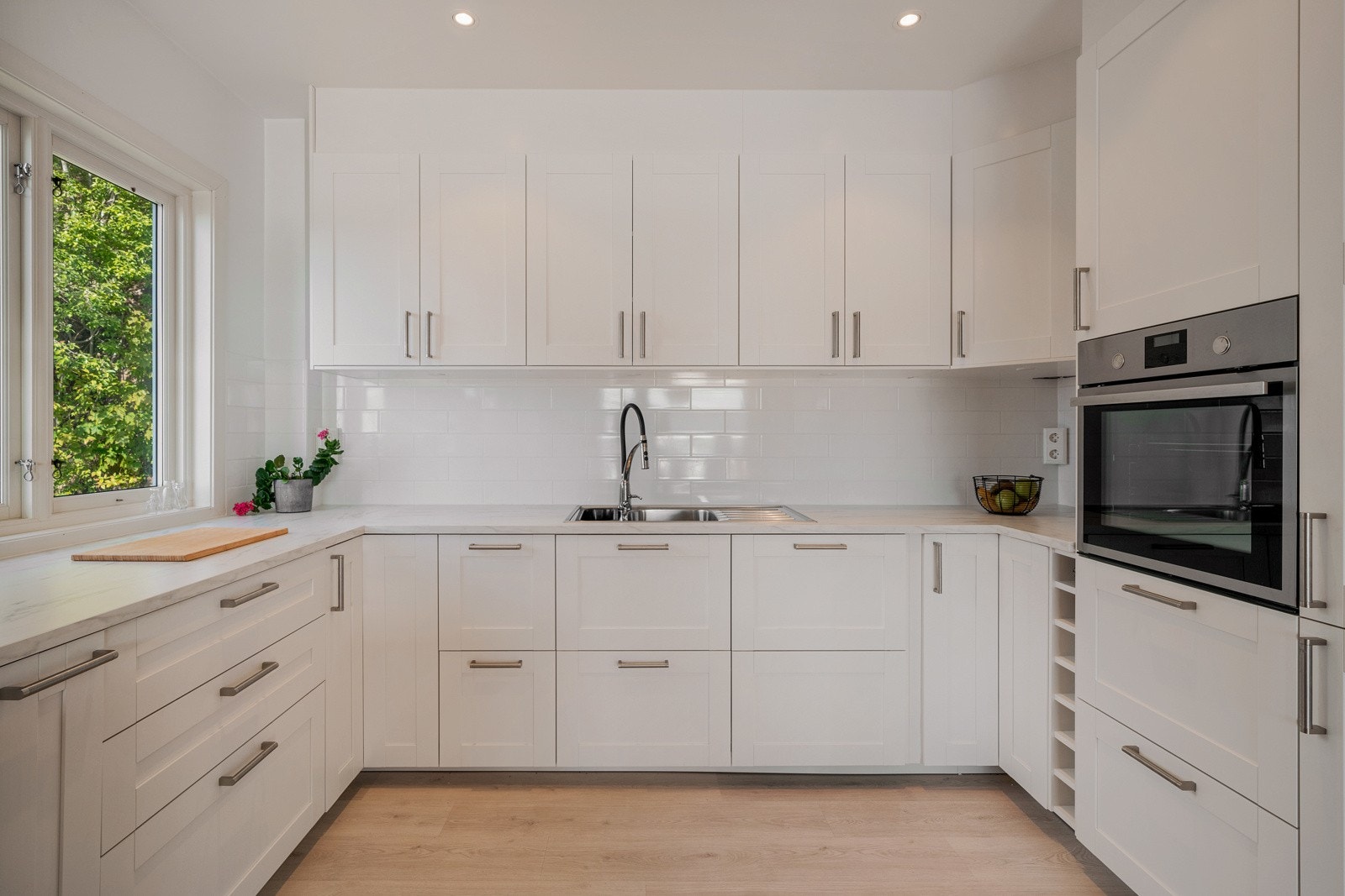 Kjøkkenet har innredning fra Ikea med hvite profilerte fronter og fliser over laminert benkeplate Galleribilde