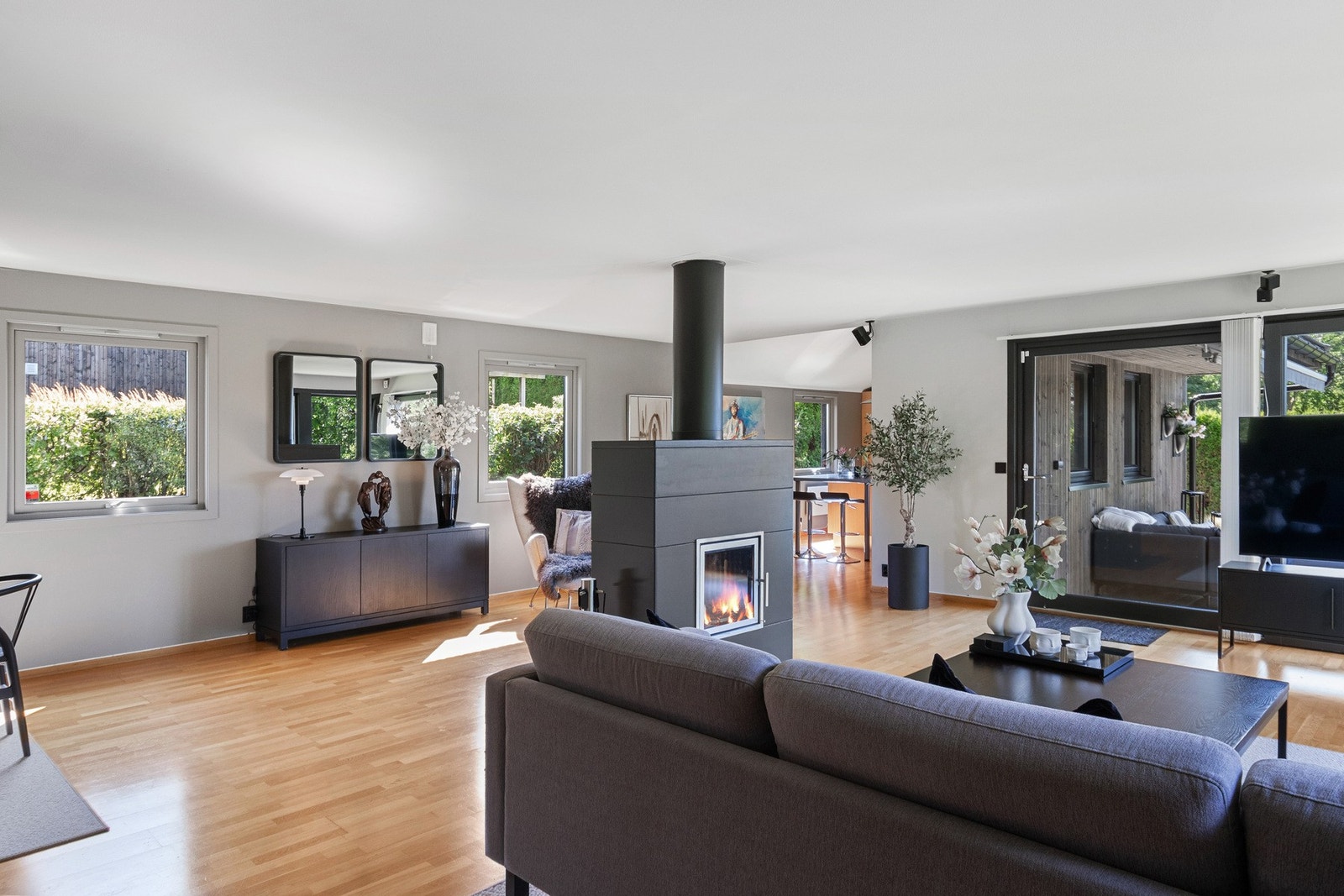 Veggene er malt i en smakfull gråtone som fremhever parkettgulvet, og sentralt i rommet er det en oppmurt peis med gjennomgående innsats. Galleribilde