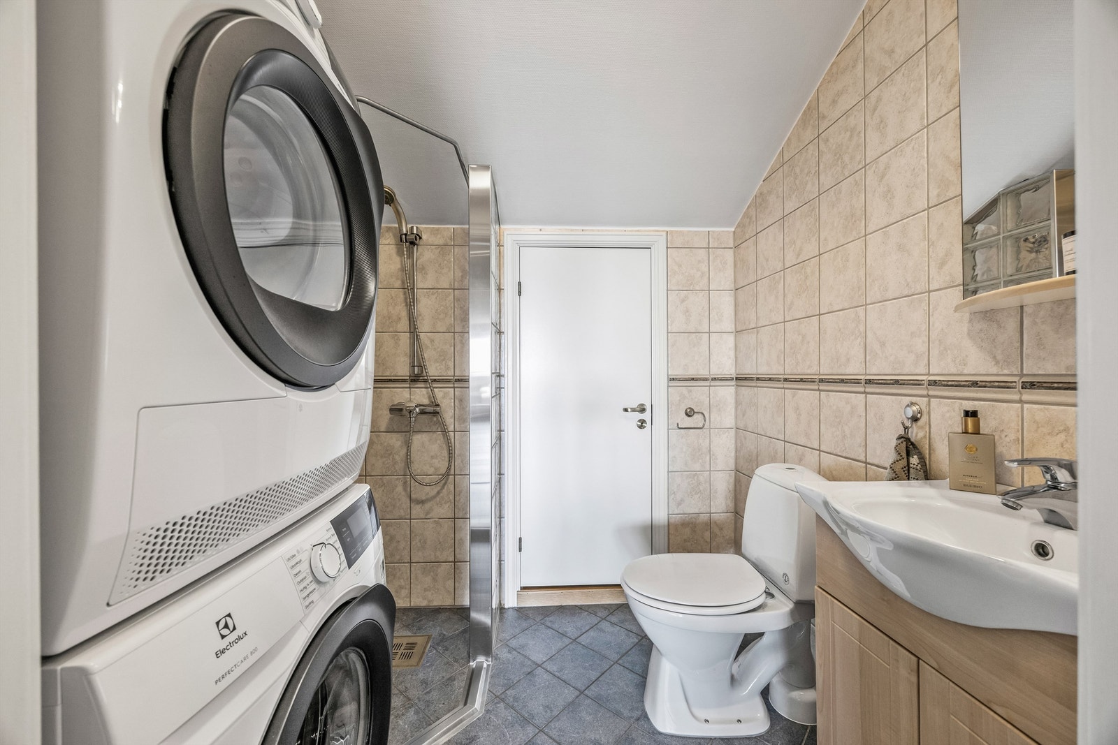 Flislagt bad med dusjhjørne, servant med innredning, speil og mekanisk avtrekk. Opplegg for vaskemaskin og tørketrommel. Galleribilde