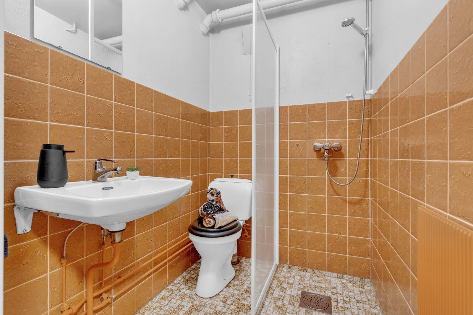 På badet i kjelleren er det dusjhjørne, servant, speil og toalett, med fliser på gulv og vegger. Baderommet har ikke blitt benyttet av nåværende eier, og trenger en oppgradering. Galleribilde