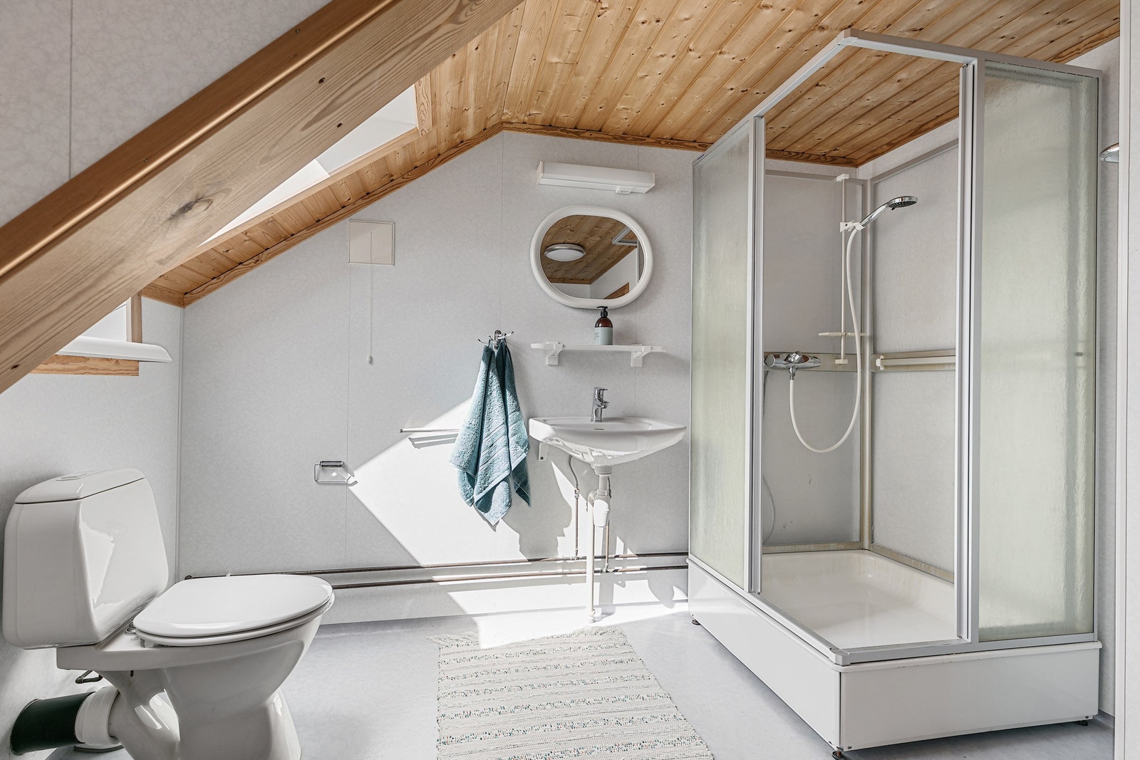 Badet i loftsetasjen er innredet med våtromsplater, gulvbelegg, dusjkabinett og toalett. En enkel servant med speil og belysning gir praktiske løsninger. Galleribilde