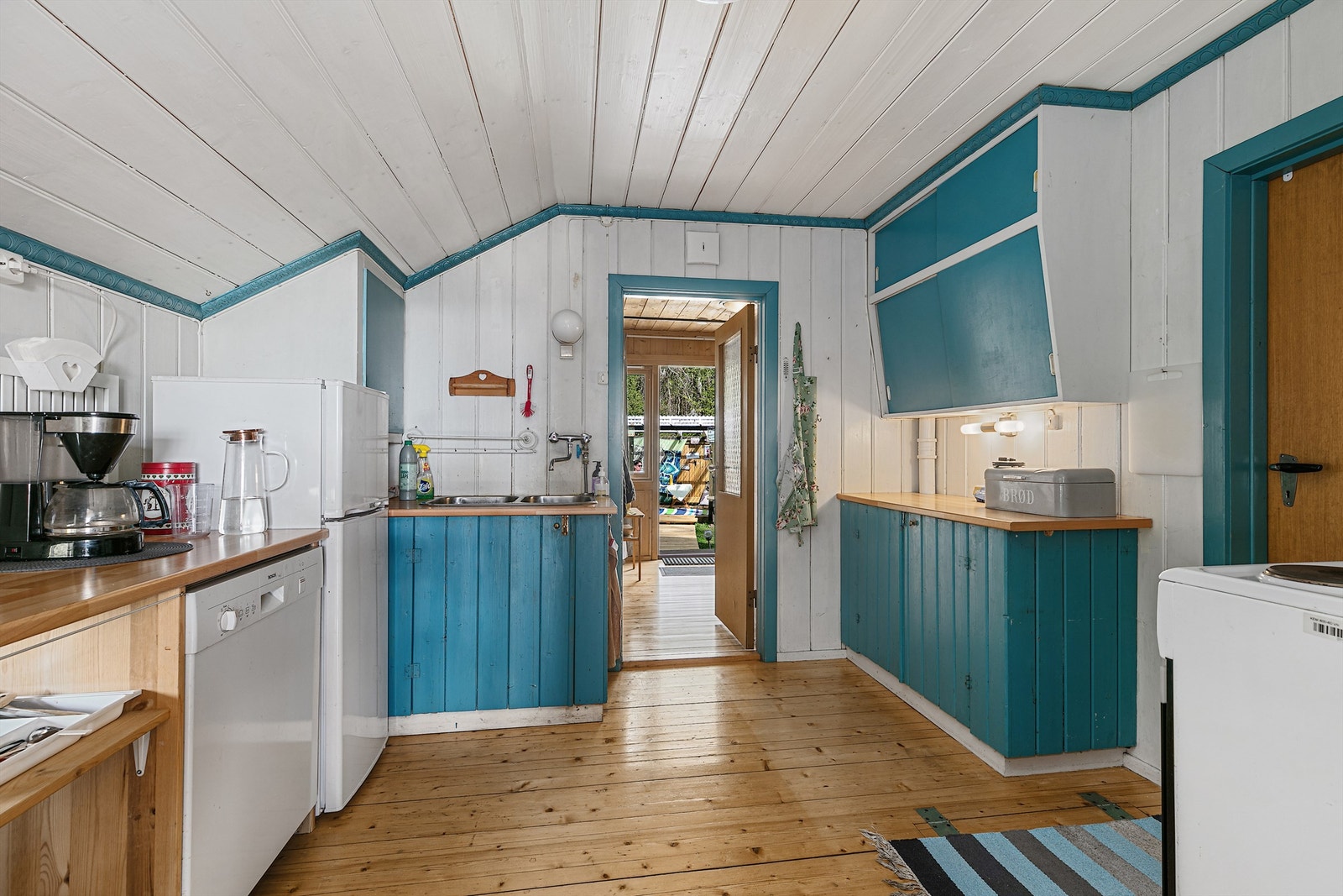 Kjøkken med tregulv, hvitmalte panelvegger og mørkeblå heltrefronter Galleribilde