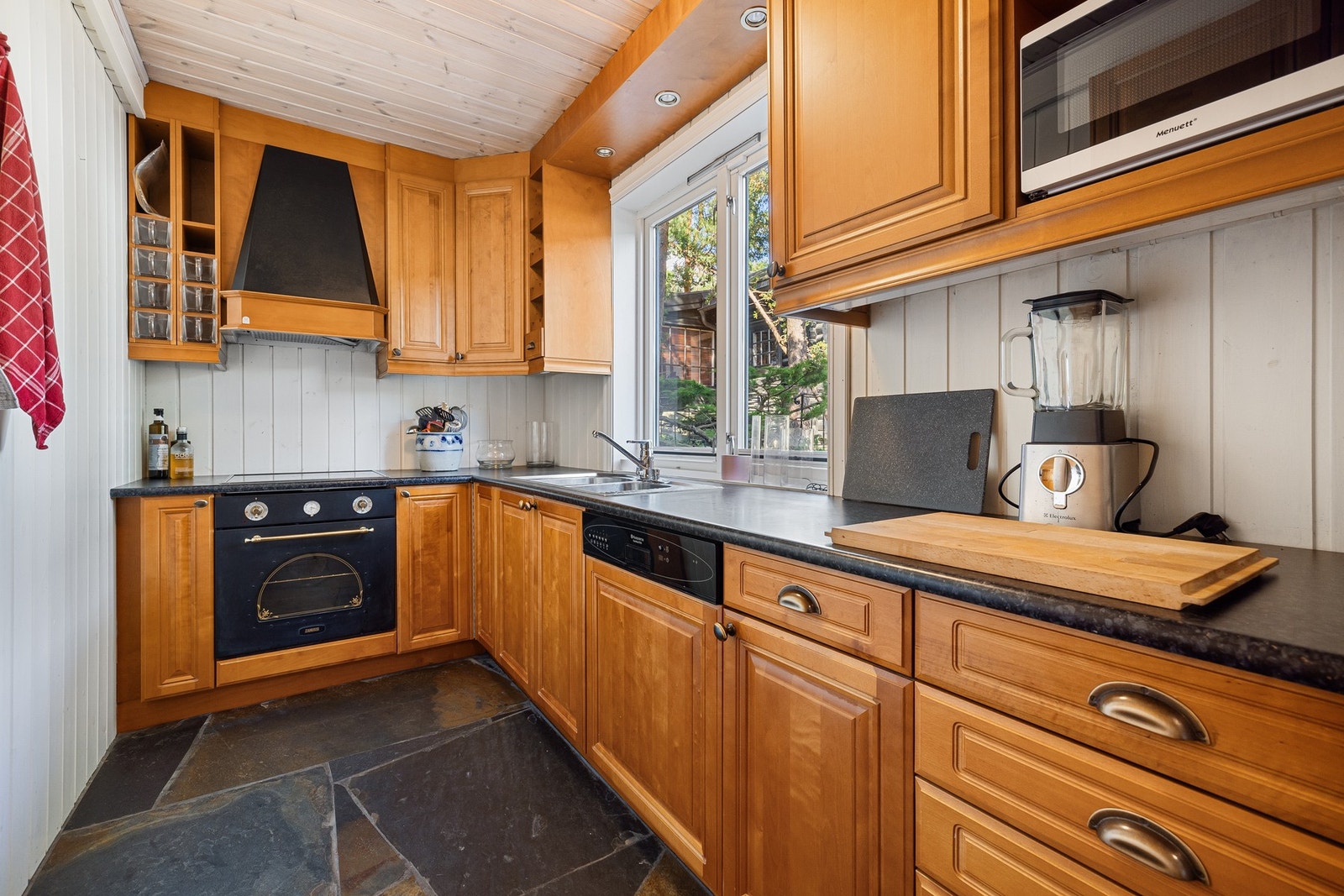 Skifergulv og profilert innredning, med integrerte hvitevarer og ventilator med avtrekk ut. Galleribilde