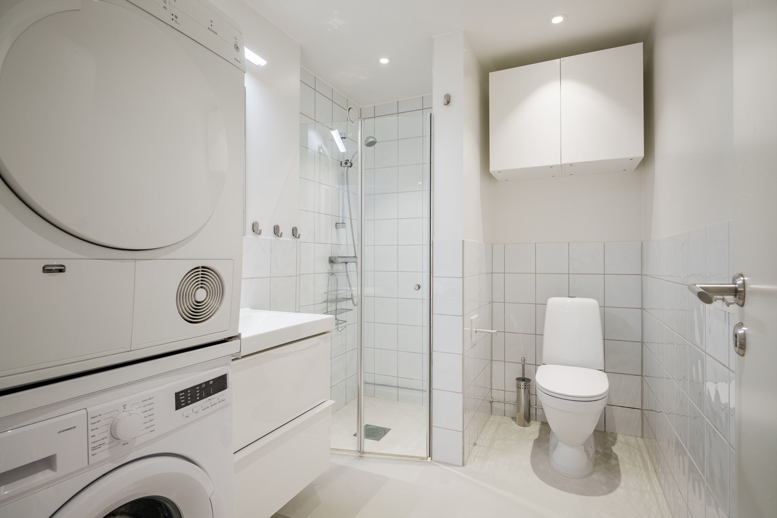 Baderom med flislagte vegger, epoxybelagt gulv, servant, toalett og dusjhjørne. Galleribilde