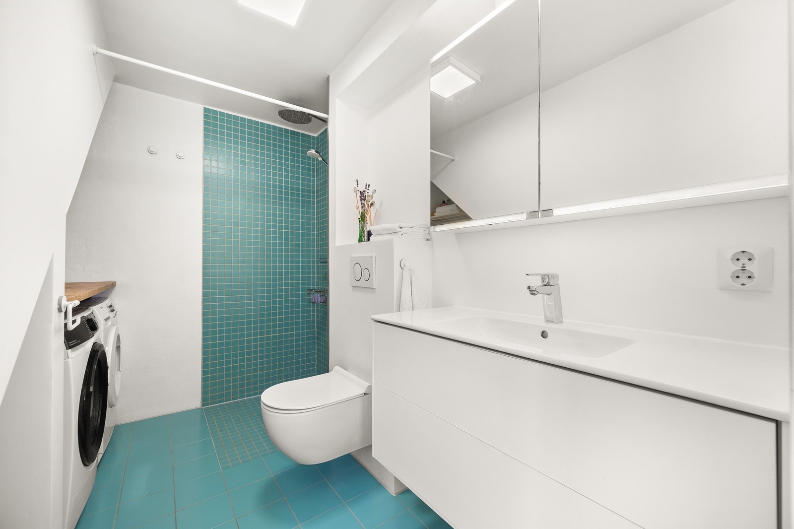 Badet i kjelleretasjen er romslig med flislagt gulv og elektrisk gulvvarme. Her er det også laget en plassbygd løsning til vaskemaskin og tørketrommel. Dette er svært praktisk i en hektisk hverdag! Galleribilde