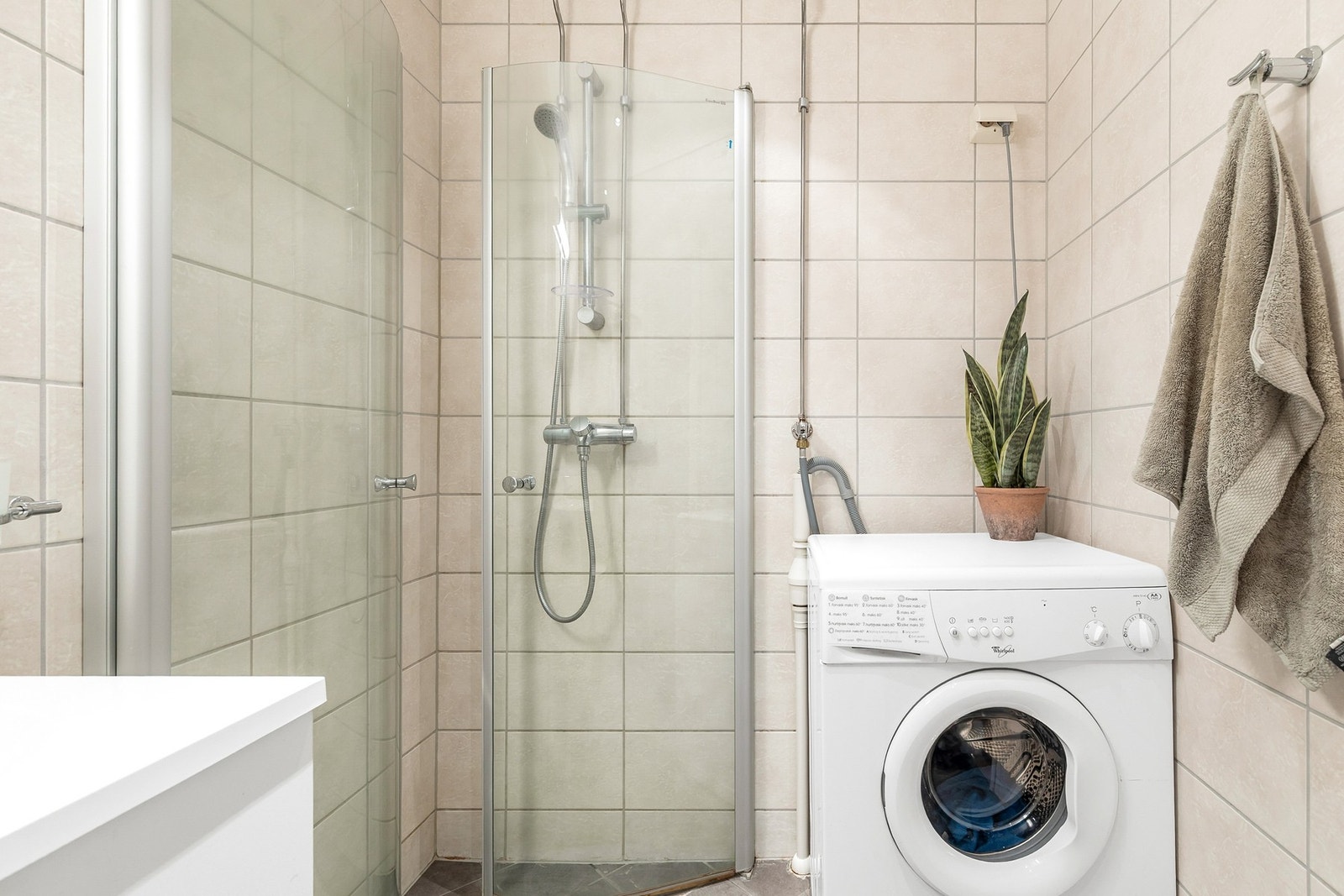 Badet er utstyrt med innredning med nedfelt servant, veggmontert toalett, dusjhjørne og opplegg for vaskemaskin Galleribilde