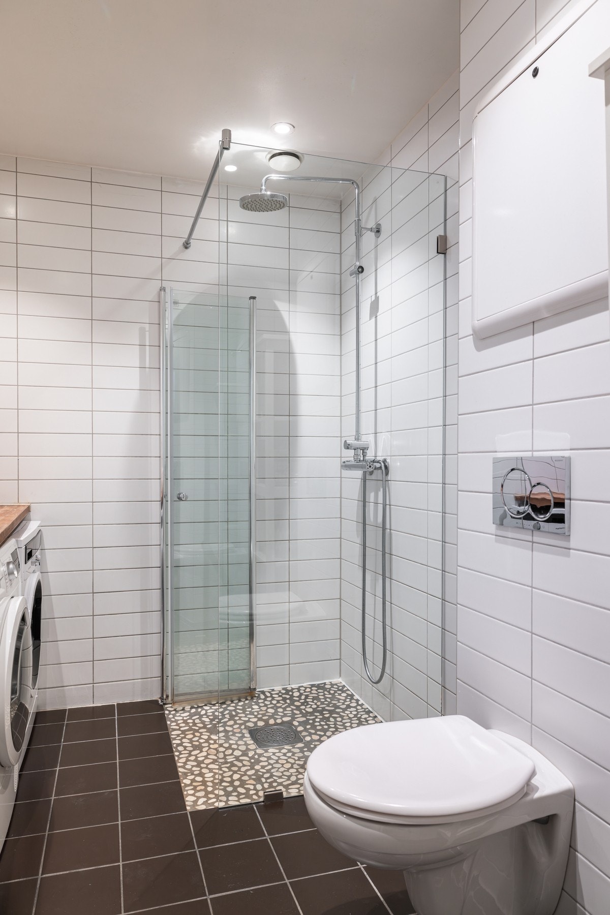 Videre er badet utstyrt med et vegghengt toalett og et dusjhjørne med regnfallsdusj. Galleribilde