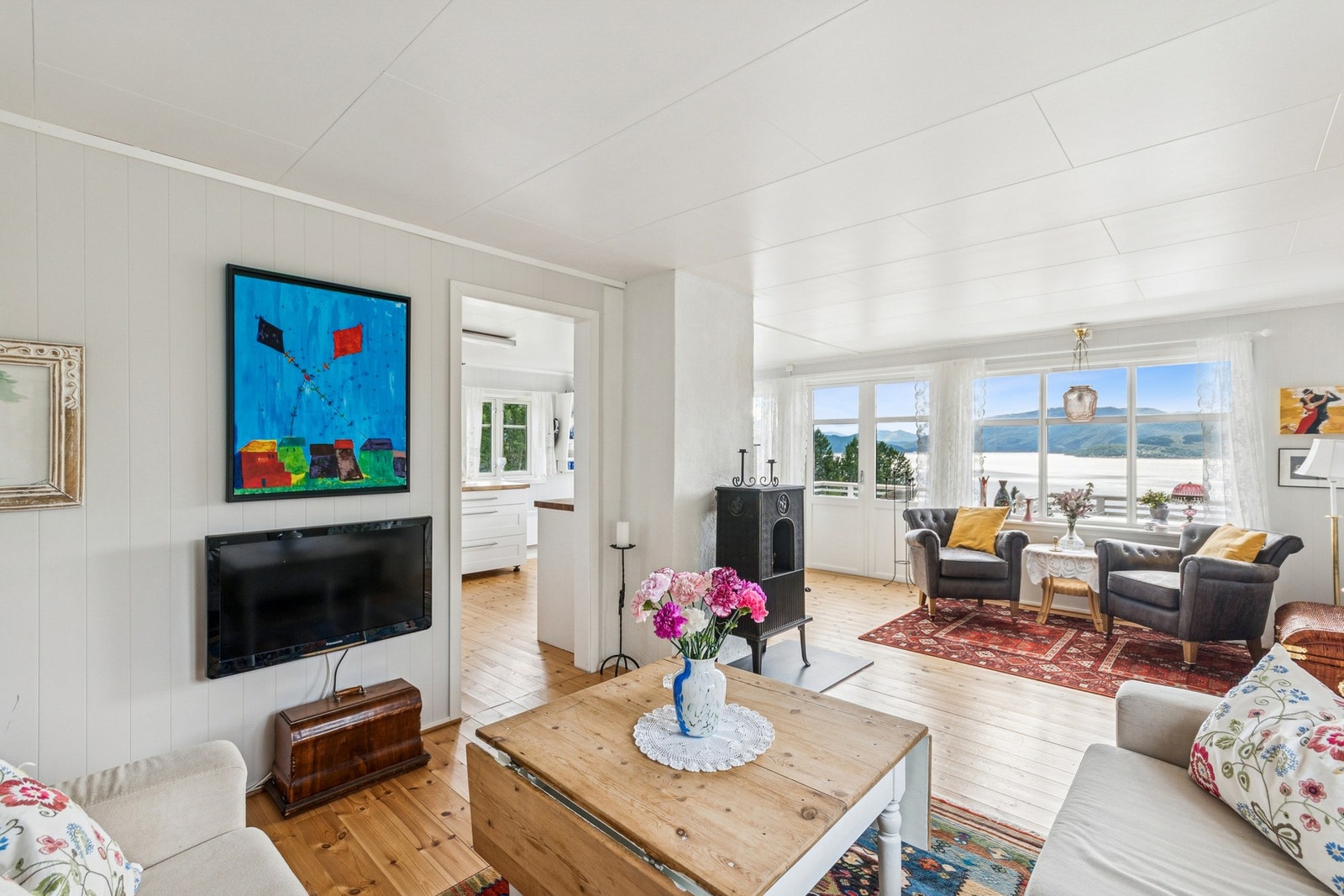 Stuen har lyse panelvegger, tregulv og store vinduer med flott utsikt mot fjorden. Galleribilde
