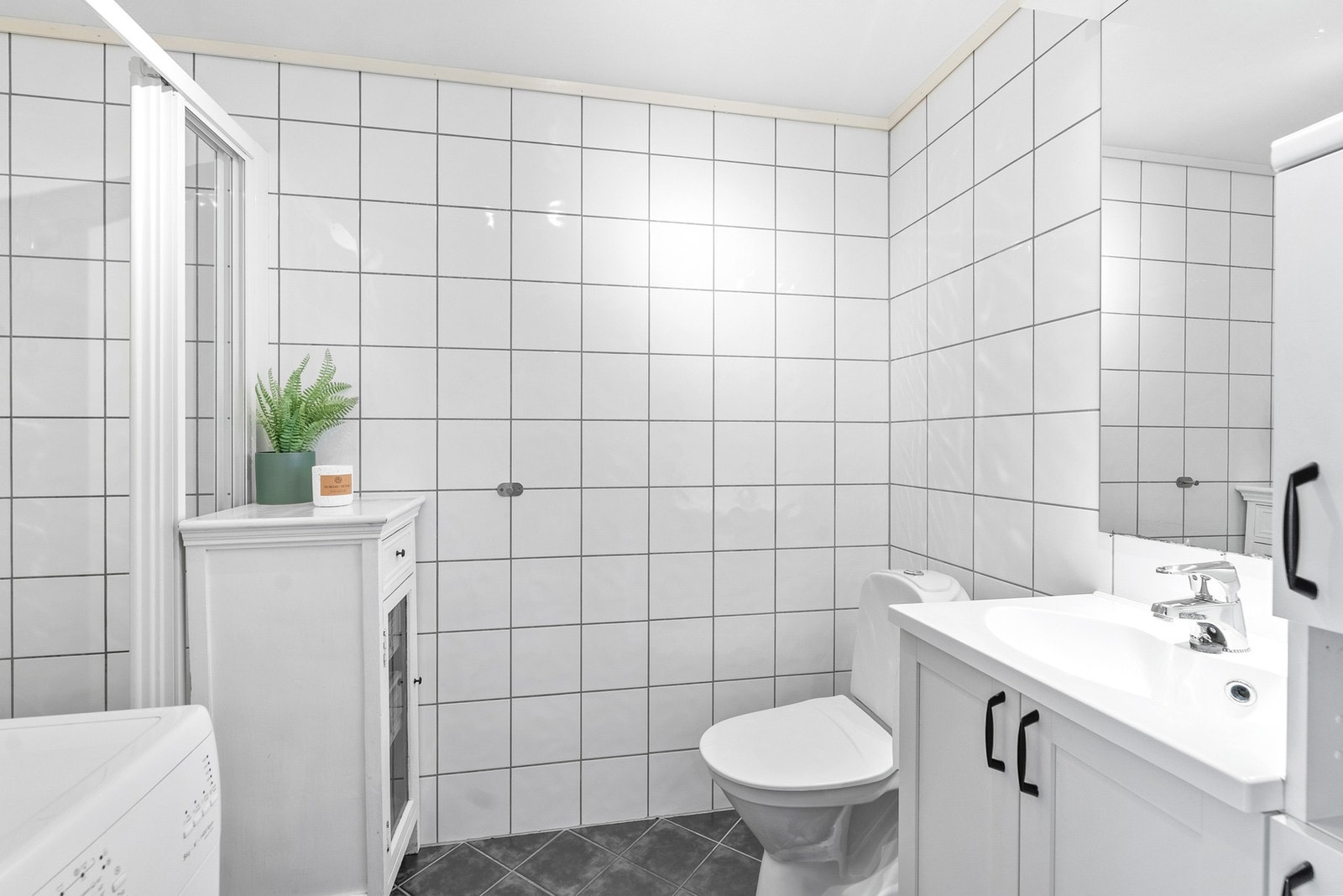 Det flislagte baderommet er utstyrt med dusjhjørne og servant. Galleribilde