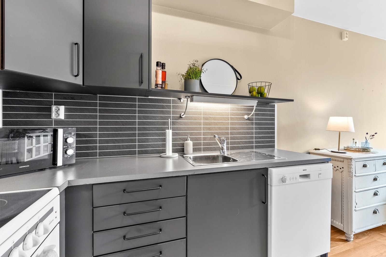 Arbeidsbenken med vask har en elegant bakvegg i mørke fliser. Belysning under overskapene sikrer optimalt arbeidslys. Galleribilde