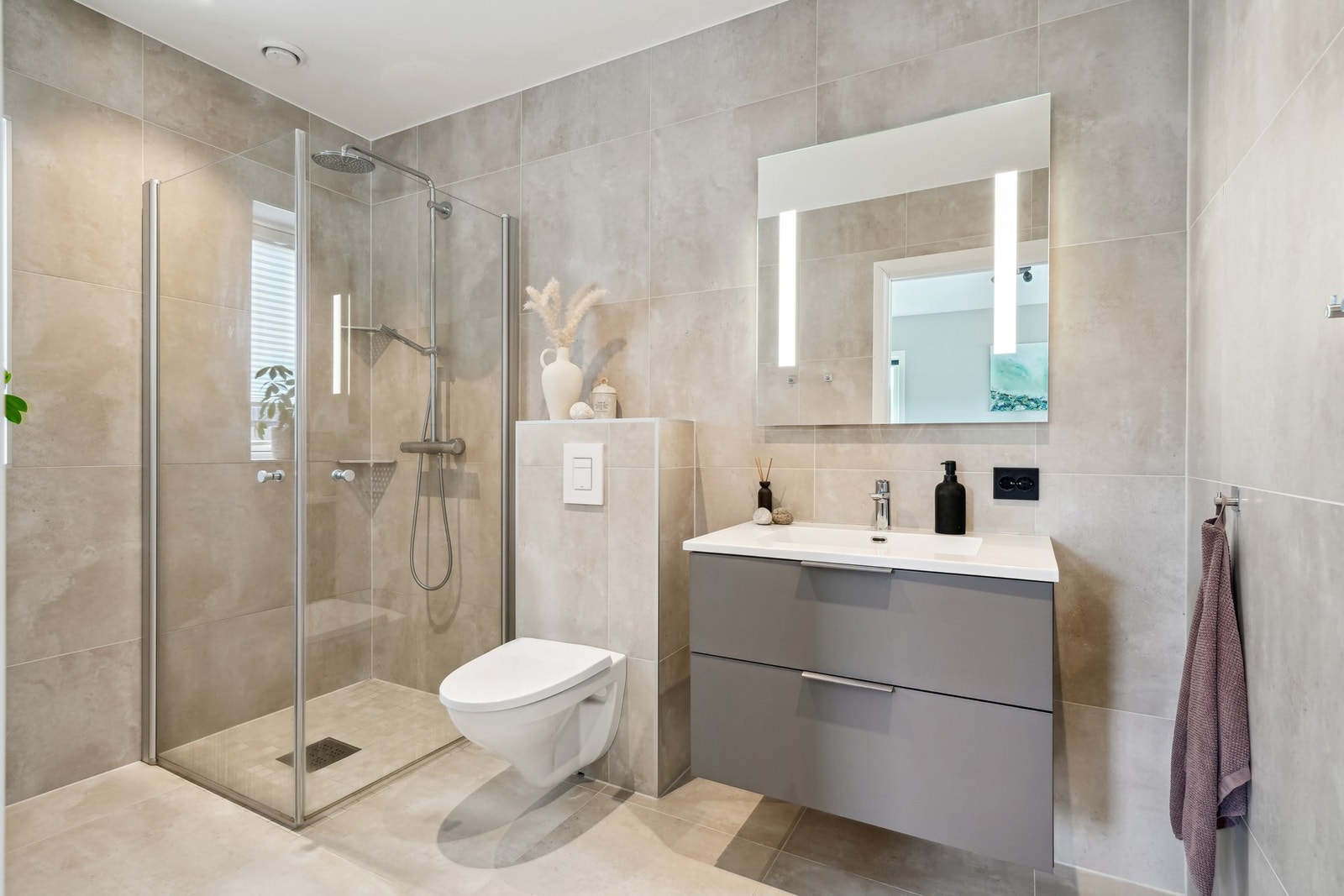 Innredet med dusjhjørne med regnfallsdusj, vegghengt toalett, servantinnredning og speil med integrert belysning. Praktisk og privat adkomst direkte fra hovedsoverommet. Galleribilde