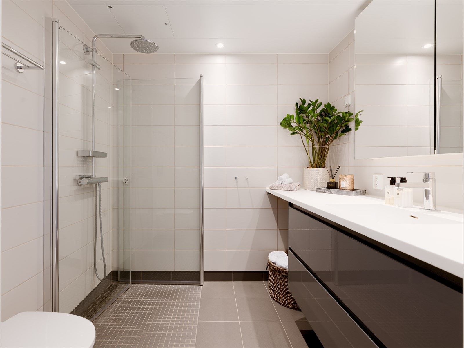 Bad II - Lyst og stilrent bad innredet med vegghengt toalett, heldekkende servant, speilskap og dusj. Opplegg for vaskemaskin. Galleribilde