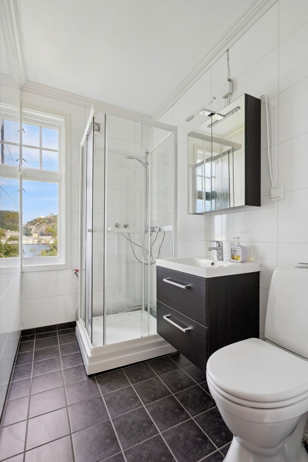 Badet er utstyrt med baderomsmøbel med skuffefronter og overliggende speil med belysning. Videre er det toalett og dusjkabinett. Galleribilde