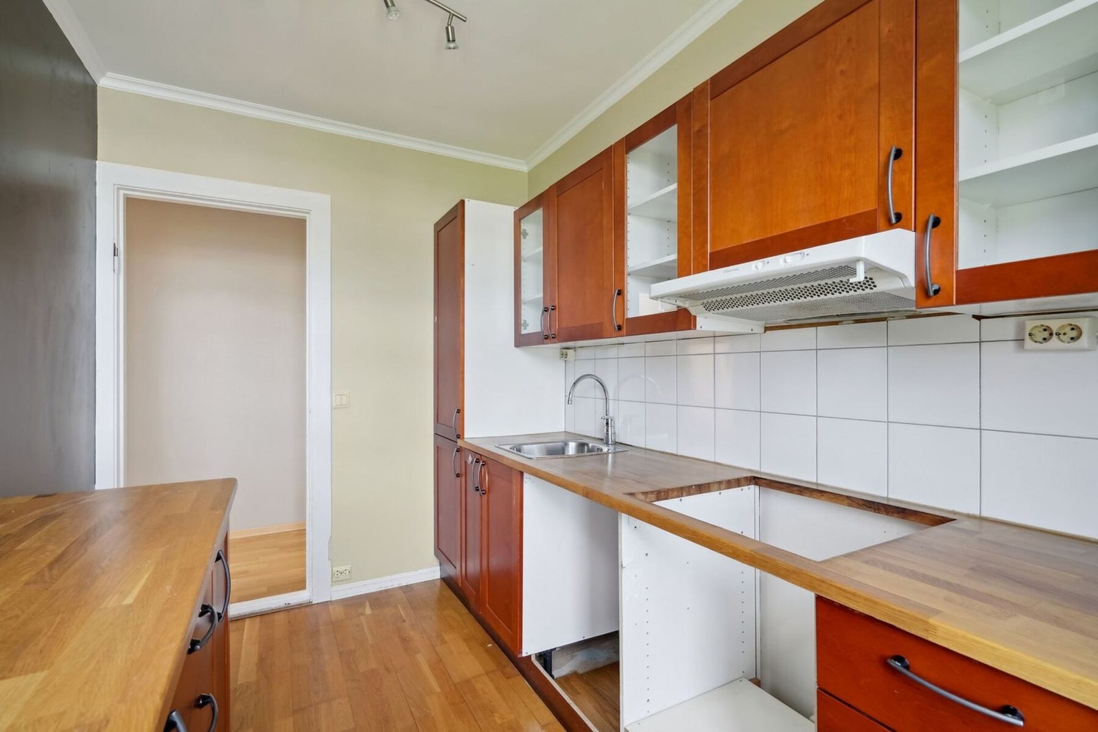 Det er fliser på vegg over benkeplaten av heltre eik. Over kokesonen er det kjøkkenventilator med avtrekk ut. Galleribilde