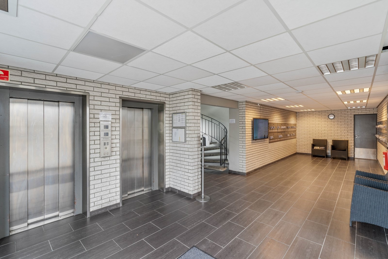 Moderne inngangsparti med heiser og sitteområde. Flott flislagt gulv og god belysning, gir et innbydende førsteinntrykk Galleribilde