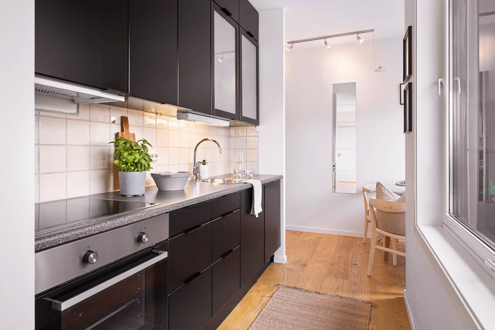 Innredningen har takhøye overskap, sorte, glatte fronter, to frostede vitrinedører og benkeplate i grå laminat med rund vaskekum i stål Galleribilde