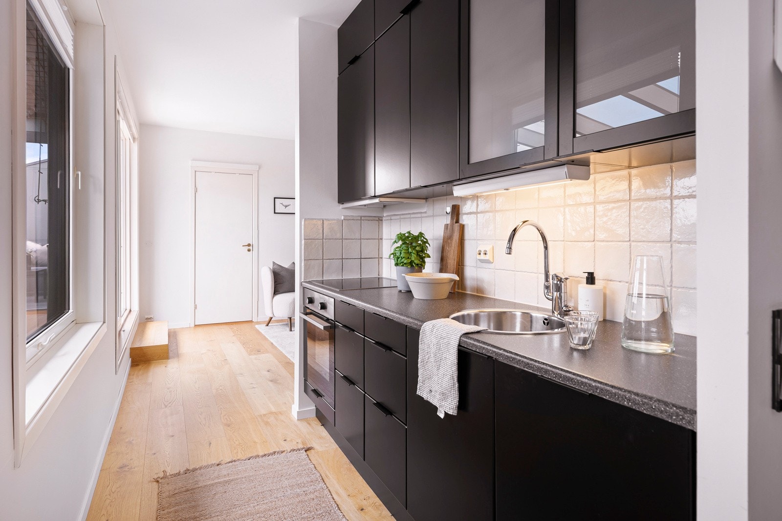 Det er ventilator over kokesonen, benkebelysning og hvite fliser som backsplash over benken. Galleribilde