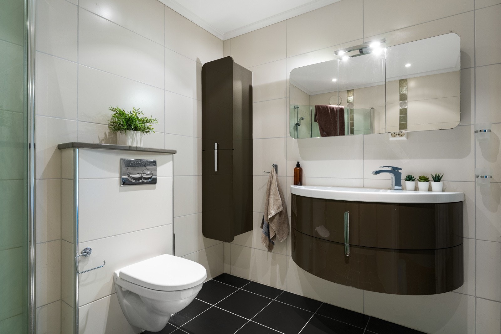 Badet er utstyrt med foldedører i dusj, veggtoalett og baderomsinnredning med heldekkende servant samt belyst speil. Galleribilde