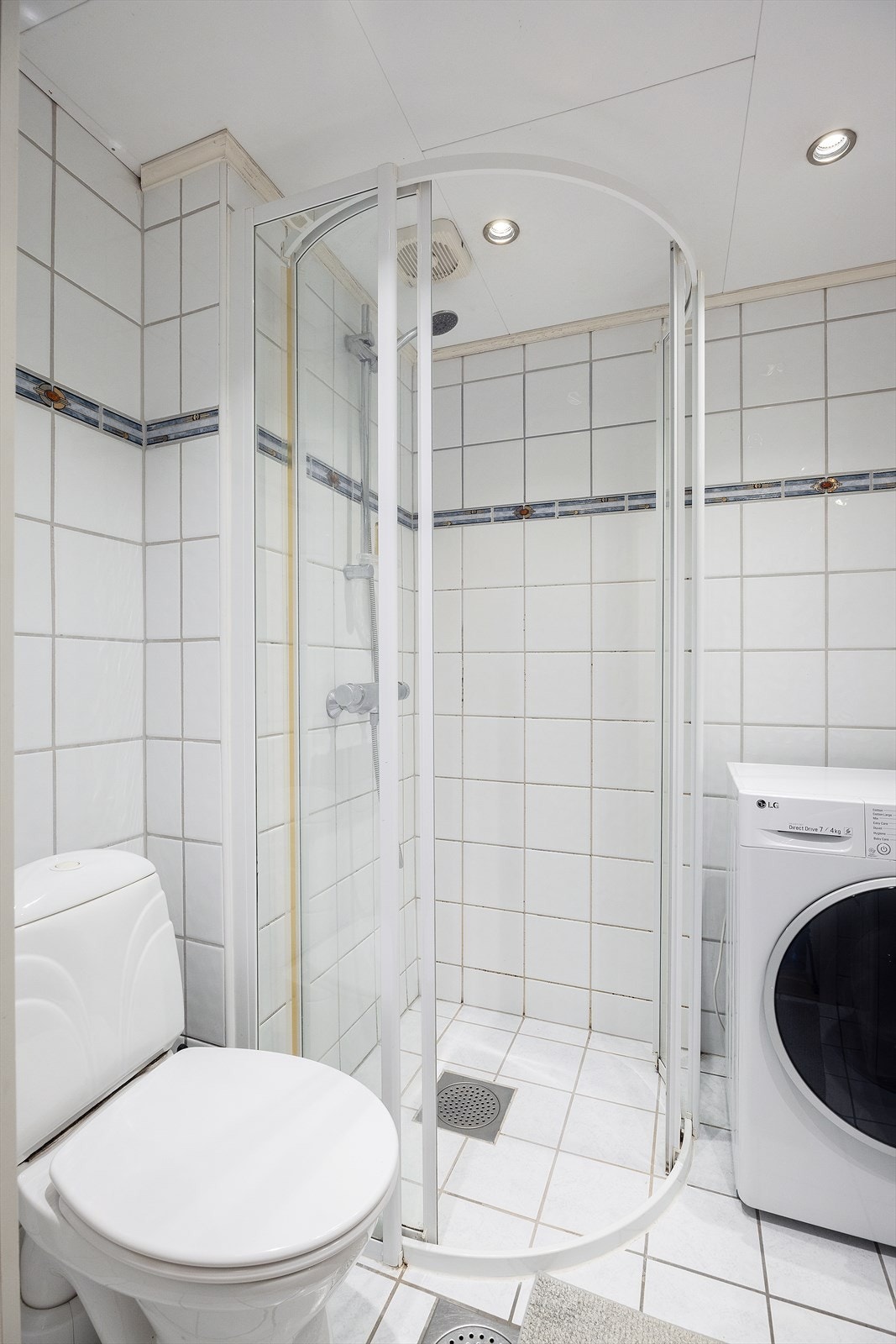 Innredet med dusj med glassdører, servant, toalett og opplegg for vaskemaskin. Galleribilde