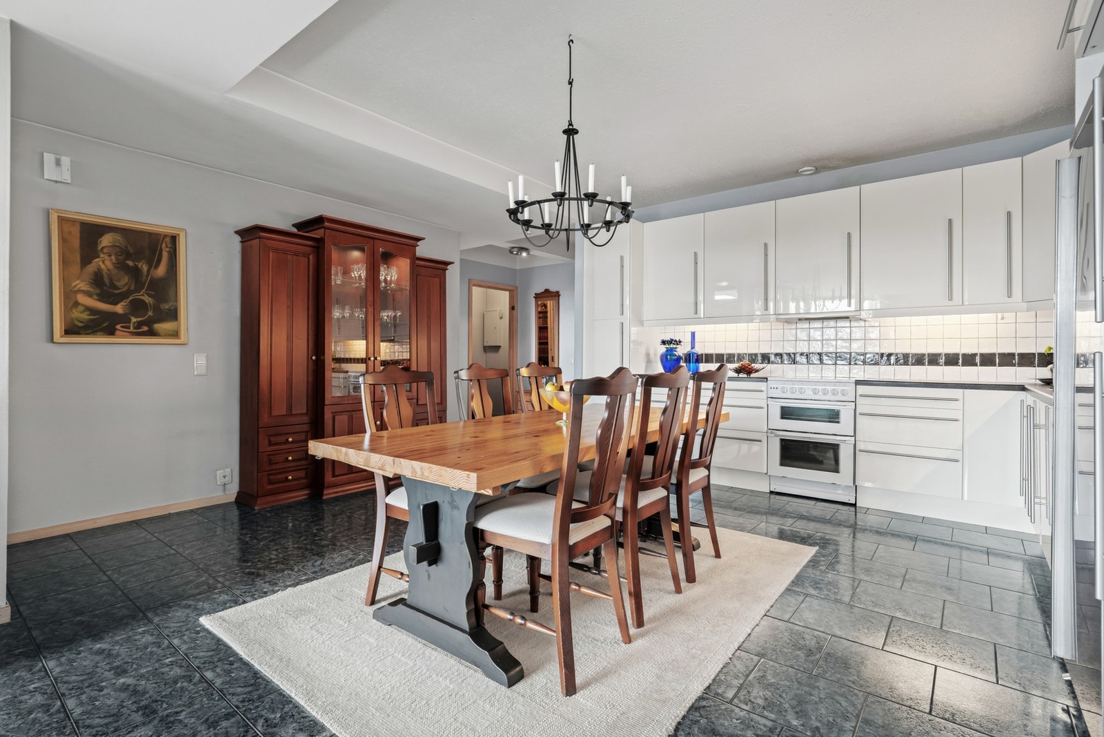 Innredningen har hvite, glatte fronter og grå laminatbenkeplate med nedfelt kum i stål. Veggene over benken er kledd med fliser, og under overskapene er det montert god arbeidsbelysning. Galleribilde