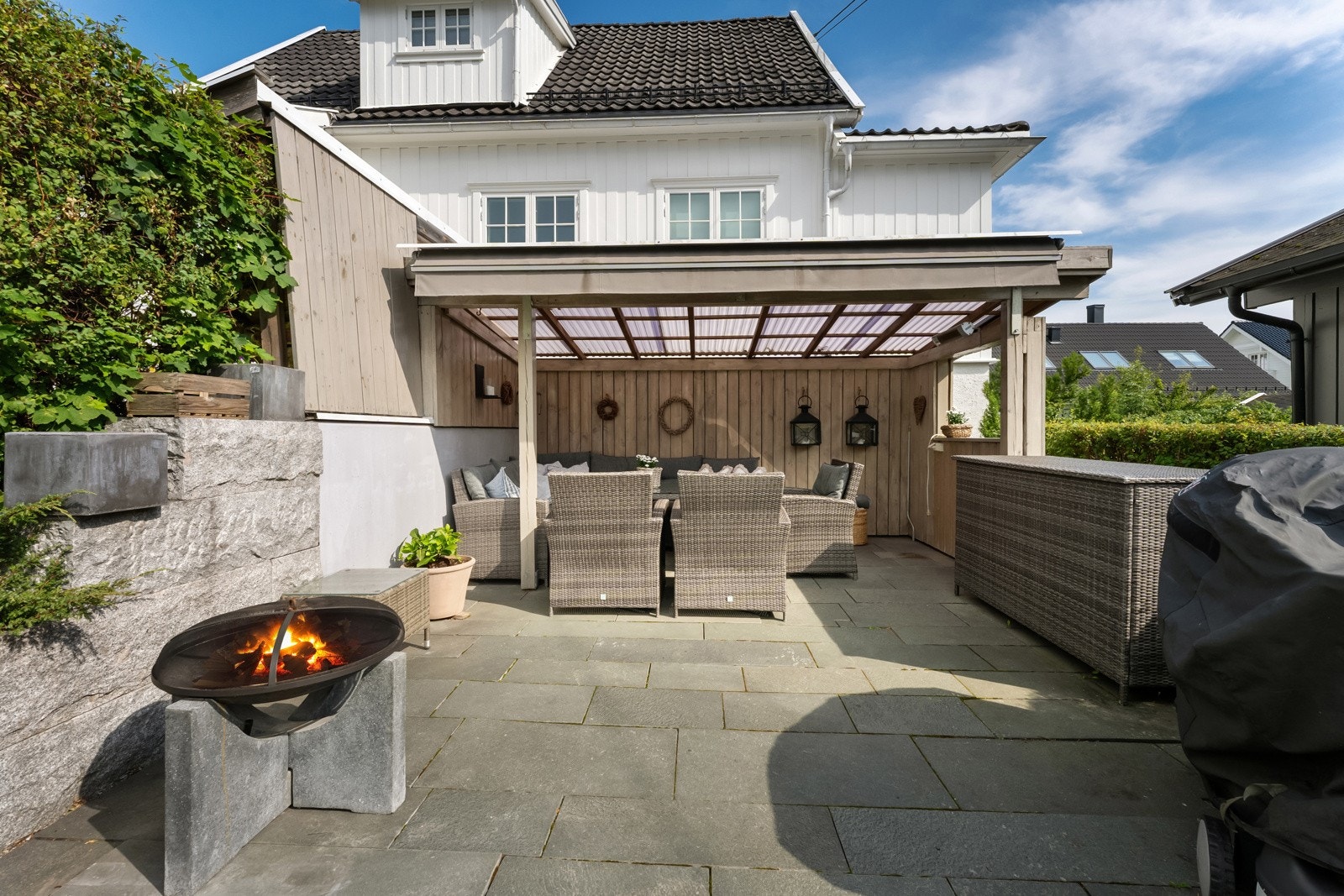 Ved inngangspartiet, på grensen mot naboen har man en flott uteplass med skiferheller og pergola. Her er det god plass til utemøbler, og den overbygde løsningen gjør sonen anvendelig uansett vær. Galleribilde