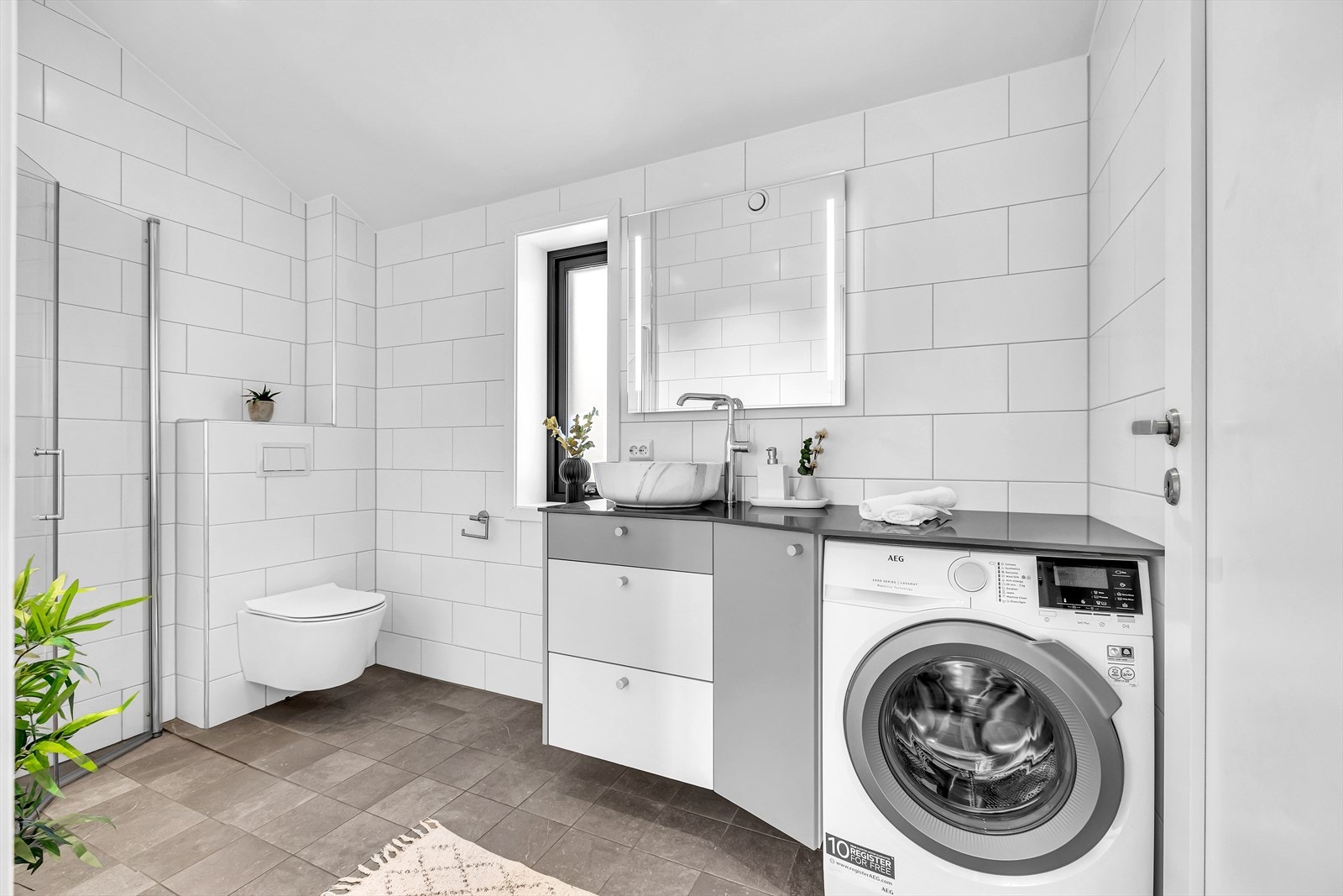 Romslig og innbydende baderom med vegghengt wc, servant med skuffer under, dusj i hjørne med innad slående dører samt opplegg for vaskemaskin. Galleribilde