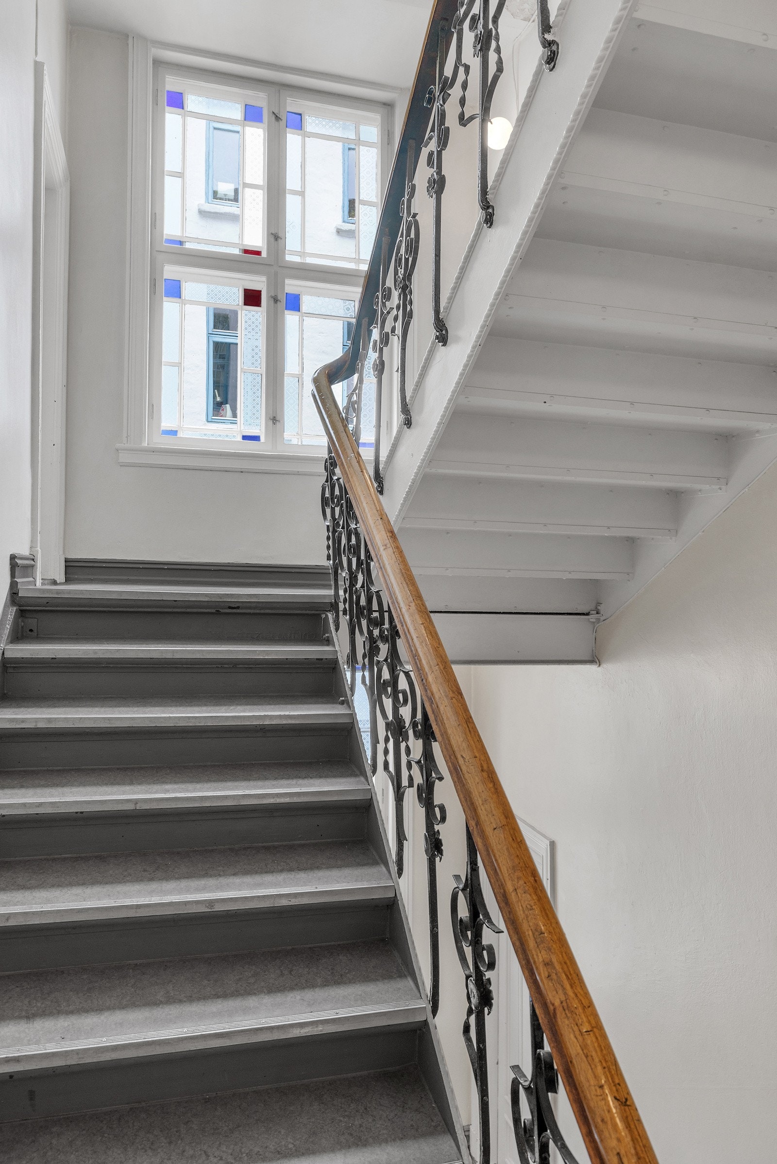 Vakker trapp med smijenrsgelender og gamle, fargerike vinduer i oppgangen. Galleribilde