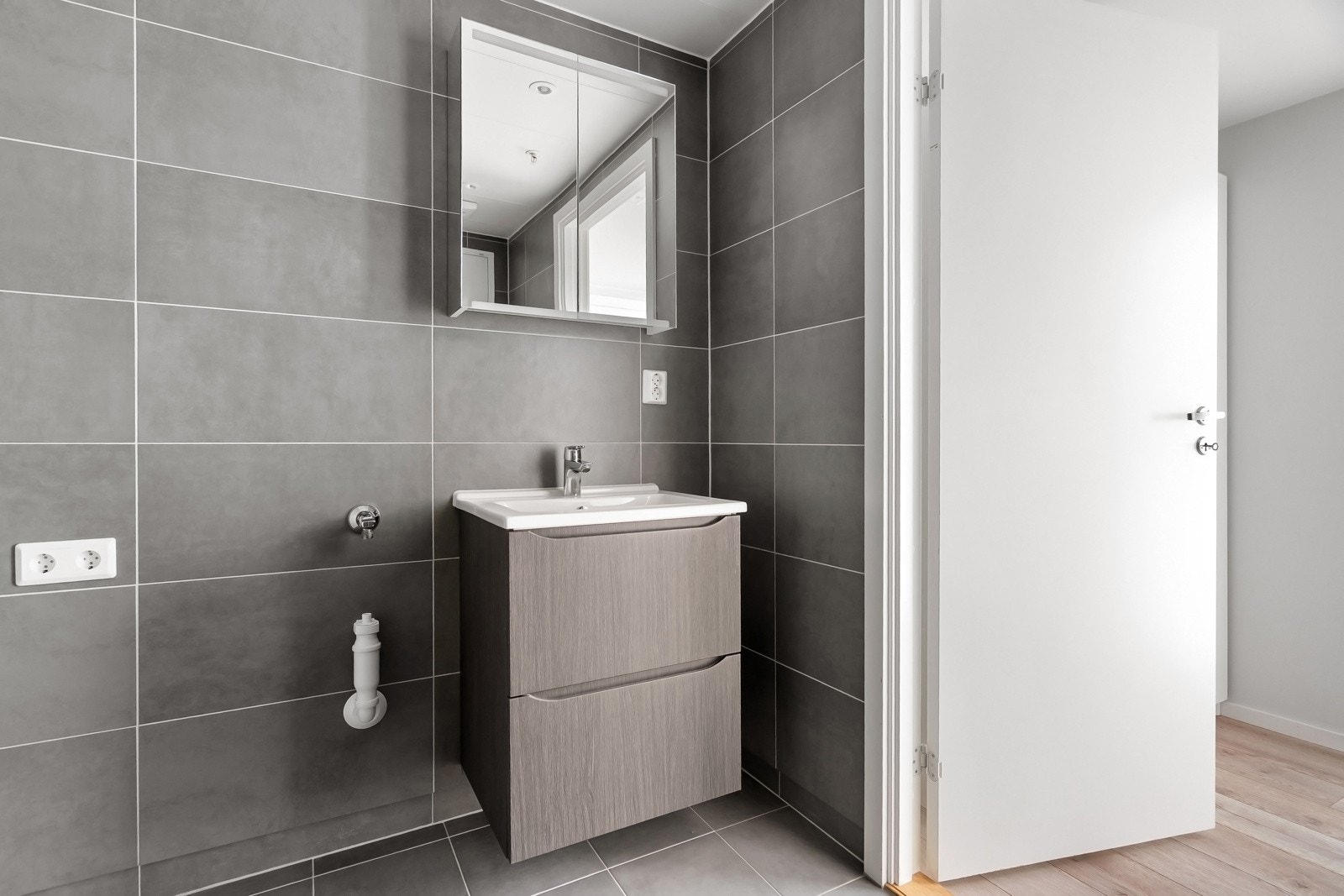 Badet har innredning med nedfelt servant, veggmontert toalett, dusjhjørne og opplegg for vaskemaskin. Tilluft via døren. Galleribilde