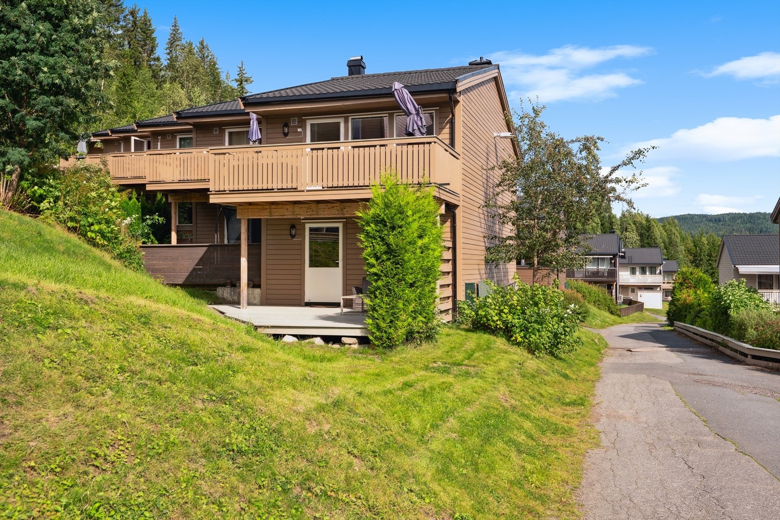 Felles festet tomt for borettslaget beliggende i et skrånende terreng, opparbeidet med plenarealer, diverse beplantning, prydbusker og trær, lekeplasser og ballbinge. Galleribilde