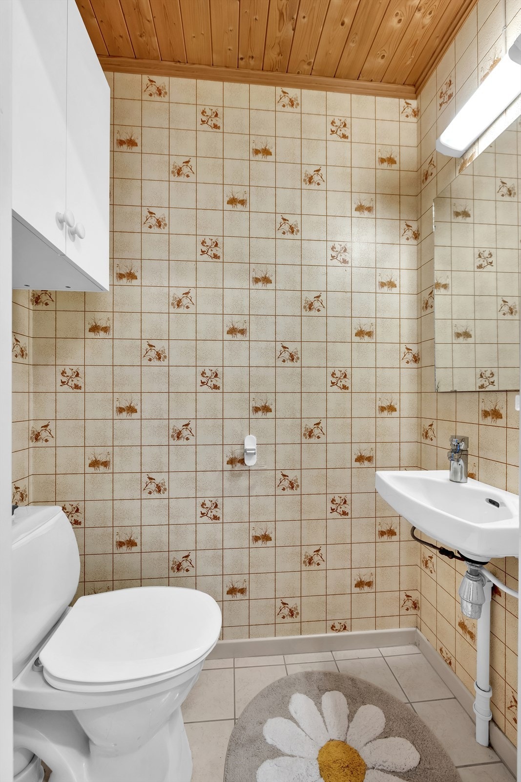 Toalettrommet ligger integrert i vaskerommet og har fliser på gulv, servant, speil med overbelysning, gulvstående toalett og et vegghengt skap. Galleribilde