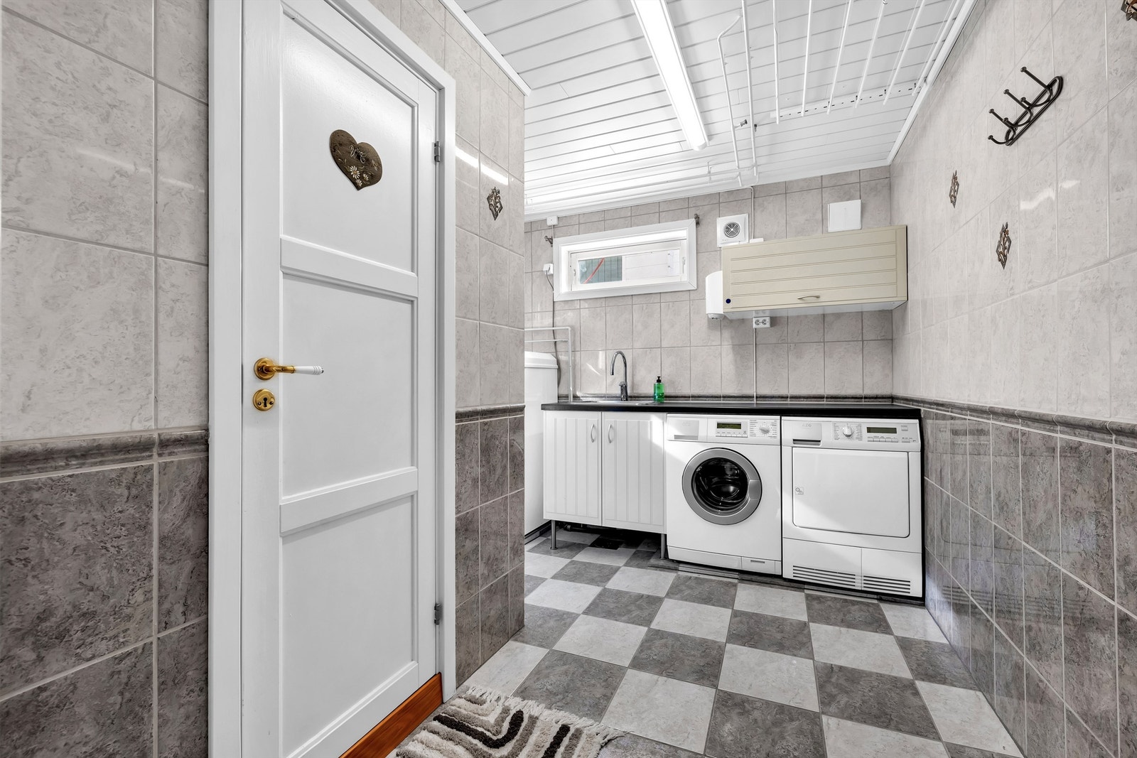 Her er det også et dusjhjørne med glassdører og veggmontert dusjarmatur, opplegg for vaskemaskin og tørketrommel, samt varmtvannsbereder plassert i hjørne. Galleribilde