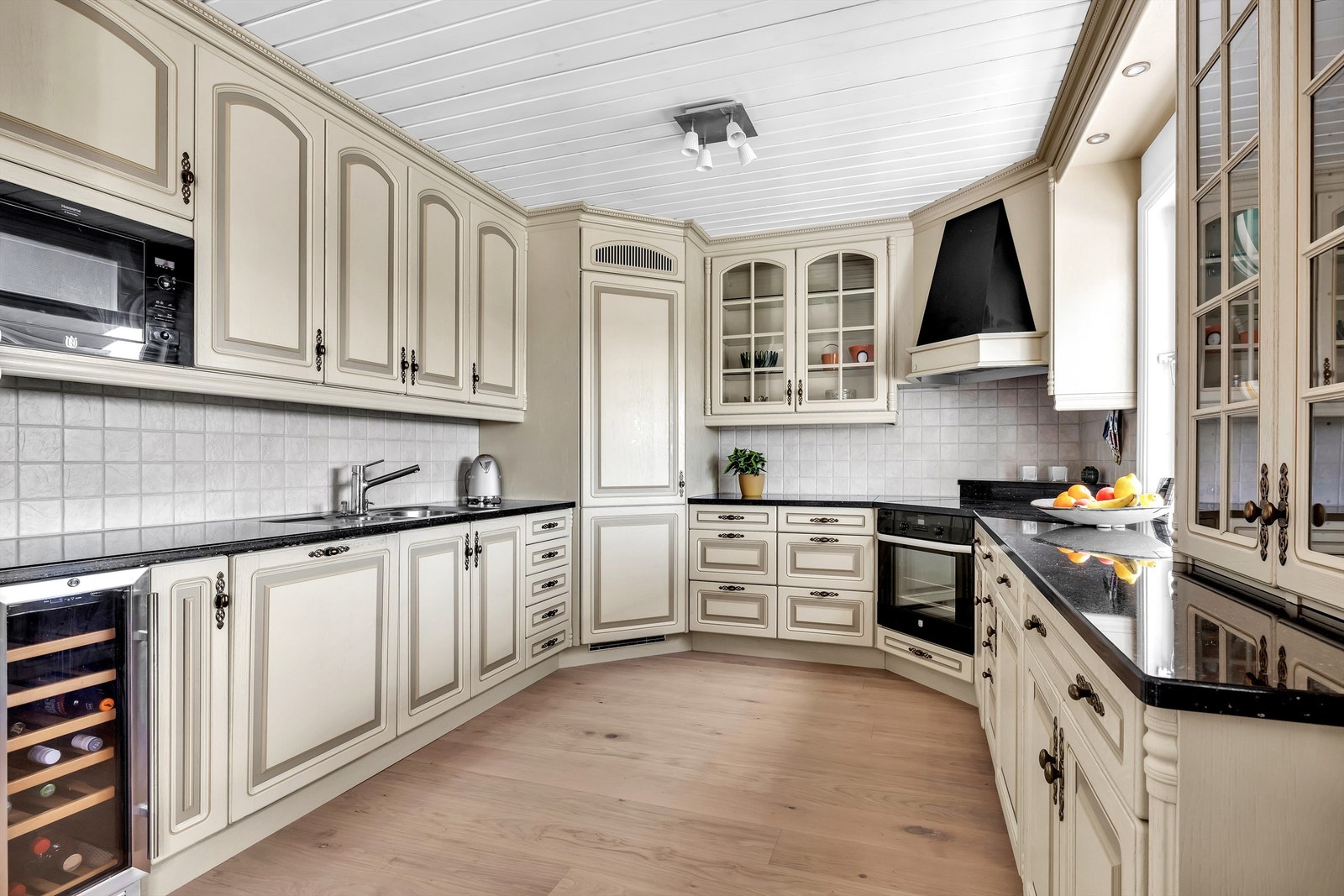 Det lyse kjøkkenet fra 2008 har en klassisk, profilert innredning, benkeplater i stein, nedfelt oppvaskkum og fliser mellom benk og overskap som gir rommet et tidløst uttrykk. Galleribilde