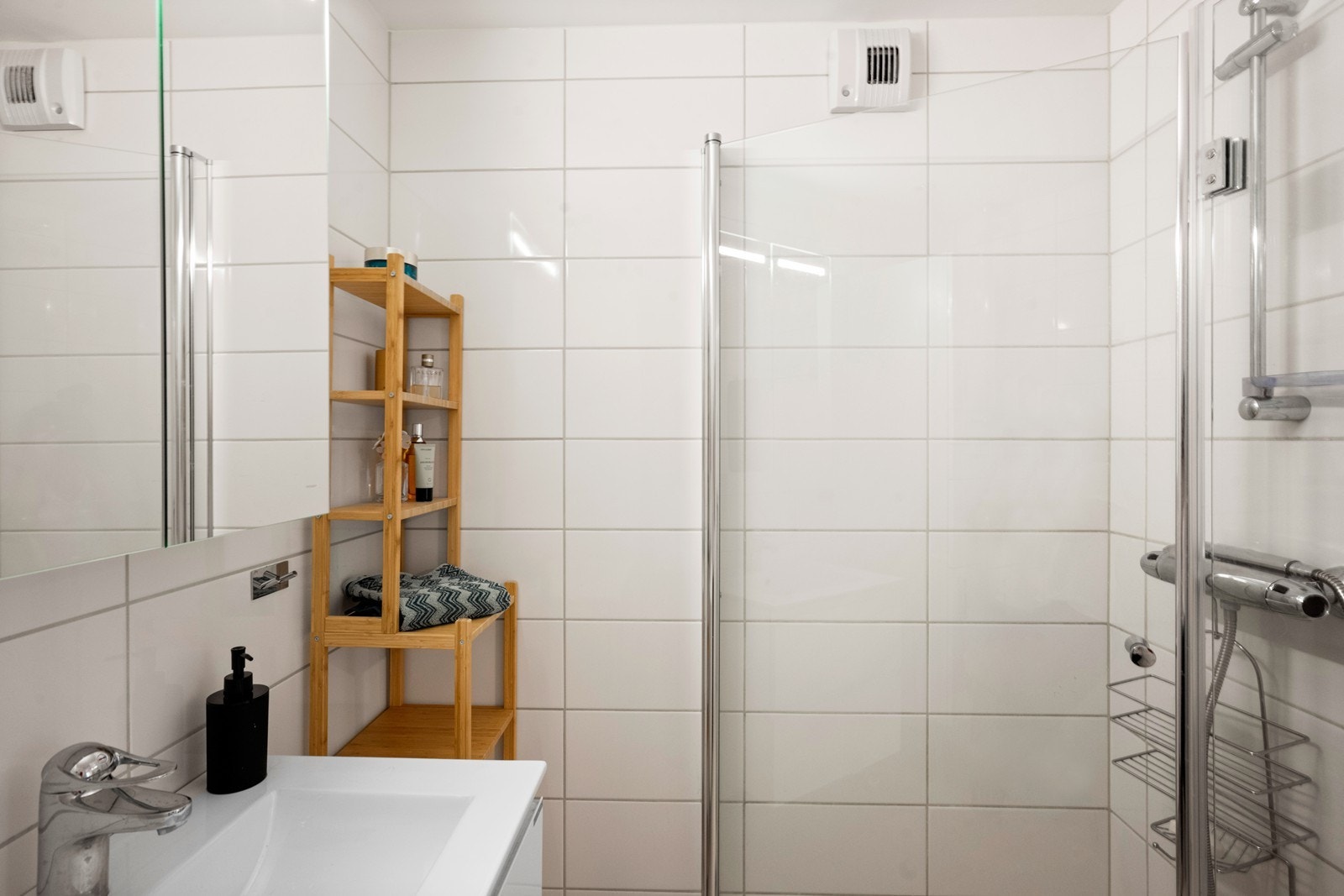 Badet er innredet med hvit baderomsinnredning med skuffer og heldekkende servant, speilskap og høyskap som gir rikelig med oppbevaringsplass. Dusjen har innfellbare dører som gir en praktisk og plassbesparende løsning. Galleribilde