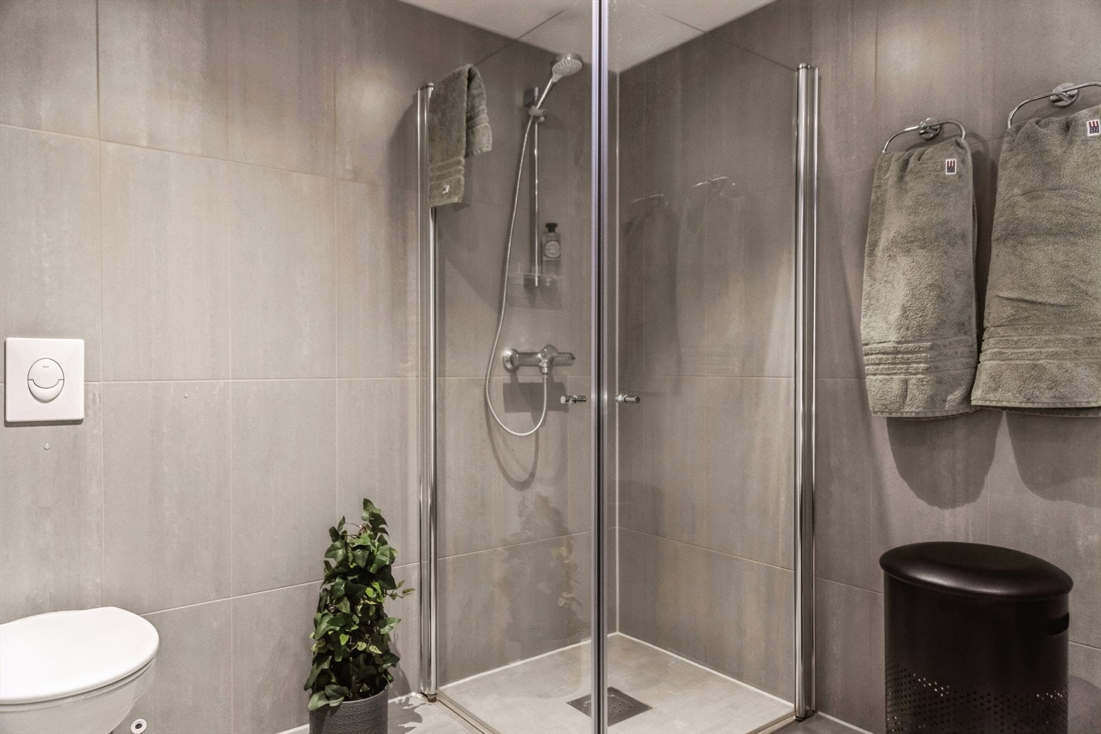 Badet utstyrt med baderomsinnredning med nedfelt servant, veggfestet toalett og dusjhjørne med glassdører. Det er vannbåren gulvvarme og opplegg for vaskemaskin. Galleribilde