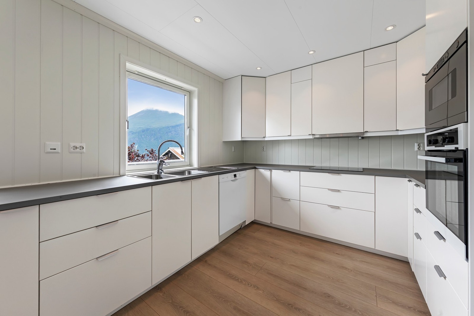 Kjøkken i kårbolig har innredning med malte fornter og benkeplate i laminat. Integrert induksjonstopp, stekeovn og mikrobølgeovn Galleribilde