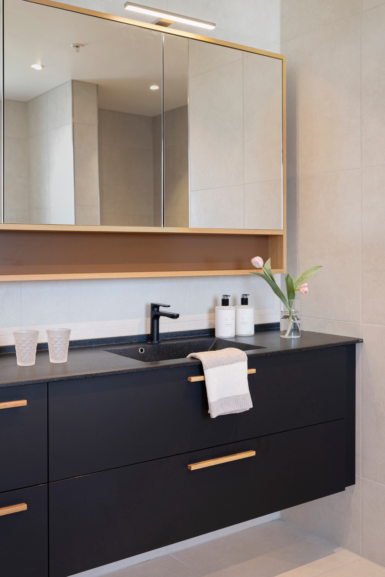 Det største badet har downlights i himlingen, store, lyse fliser på veggene og matchende fliser på gulv med vannbåren gulvvarme. Galleribilde