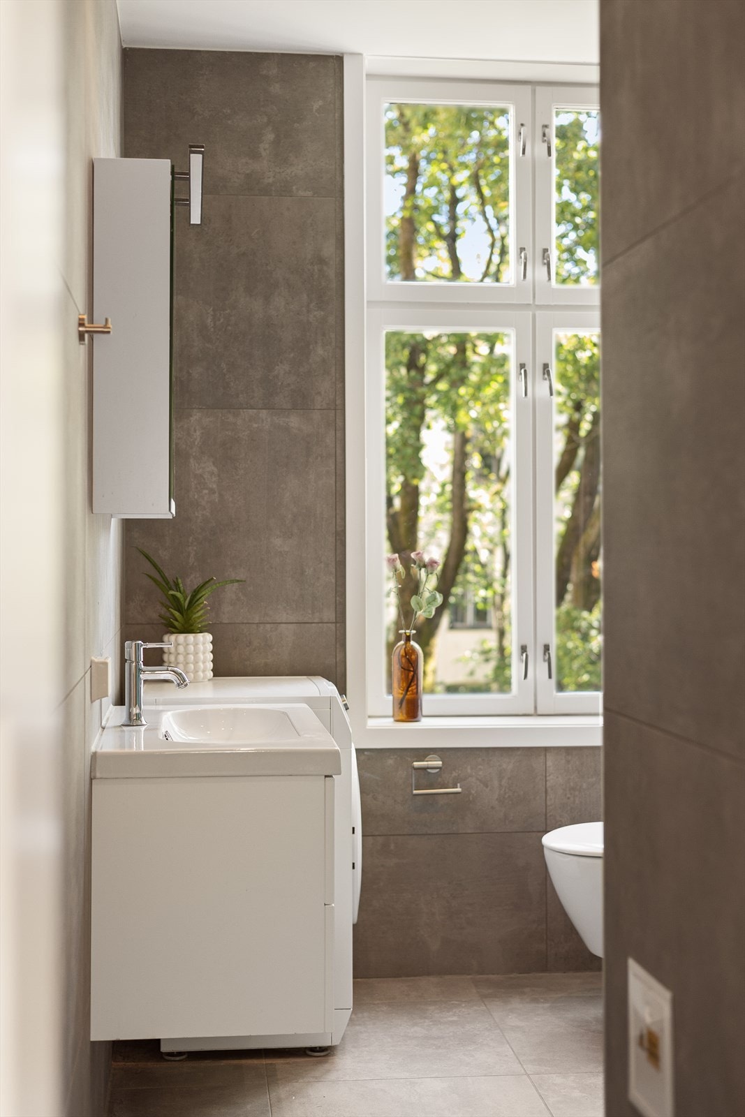 Baderommet er innredet med nedfelt servant, veggmontert toalett og dusjvegger/hjørne. Galleribilde