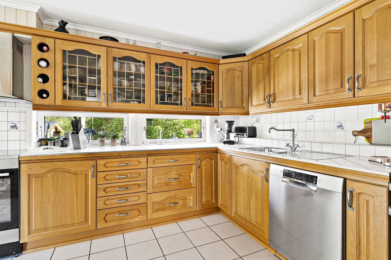 Kjøkken med profilerte fronter og fliser på benkeplate og vegg over benkeplate. Galleribilde