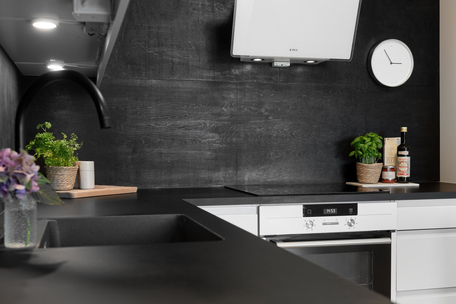 Benkeplaten av av laminat med nedfelt oppvaskkum med ett-greps kjøkkenarmatur. Det er benkeskapsbelysning og stikkontakter over kjøkkenbenk Galleribilde