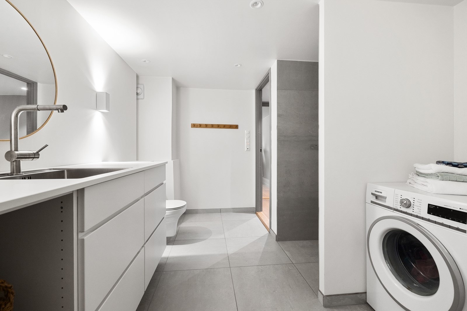 Det er varmekabler i gulv samt dimbare spotter som lyskilde på badet. Rommet har innredning med nedfelt servant og benkeplate av laminat, veggmontert toalett, dusjhjørne samt opplegg for vaskemaskin. Galleribilde