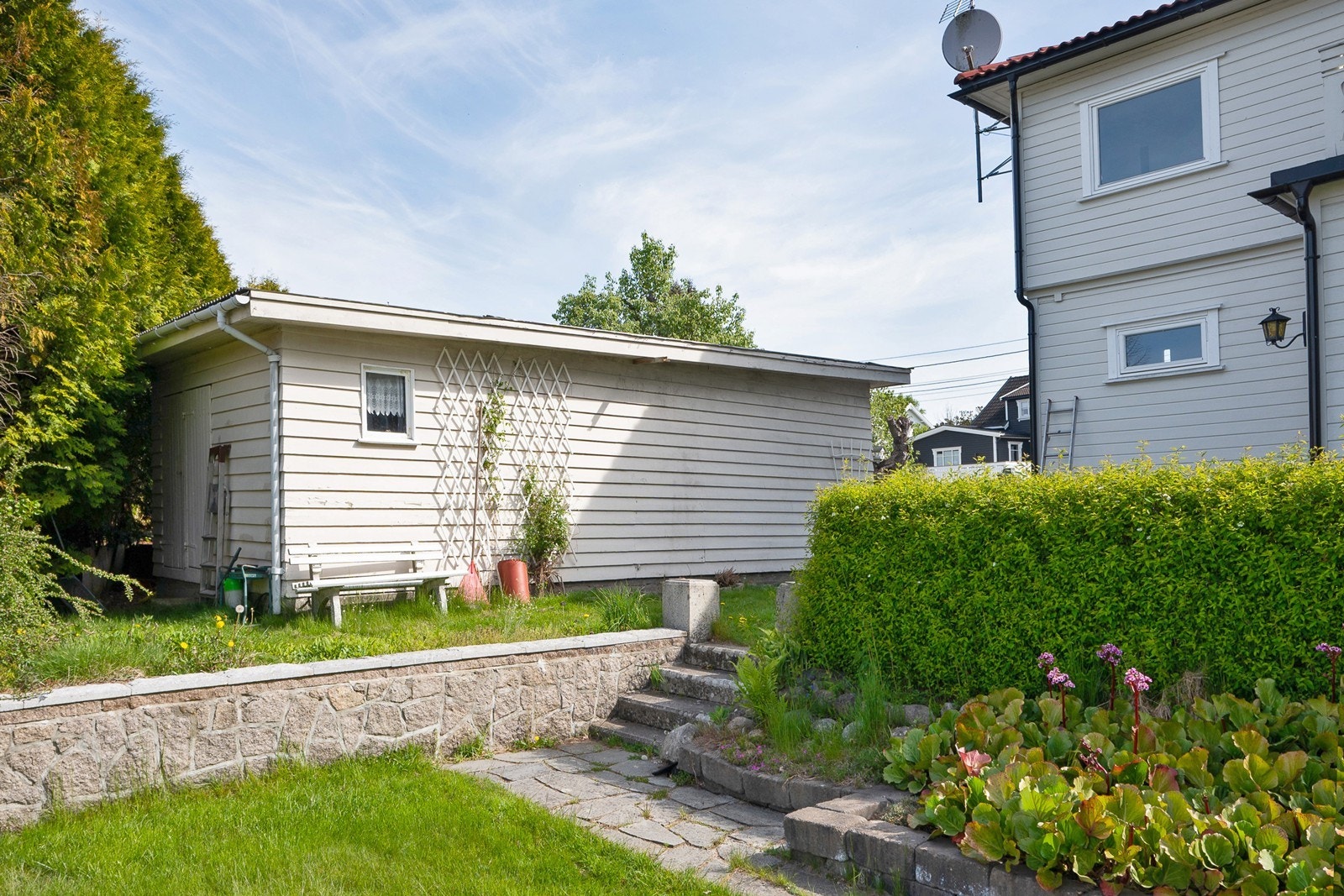 Steintrapp gir videre tilgang til hage på vestsiden, pent opparbeidet med støttemur, bed, hekk og hageplen. Galleribilde