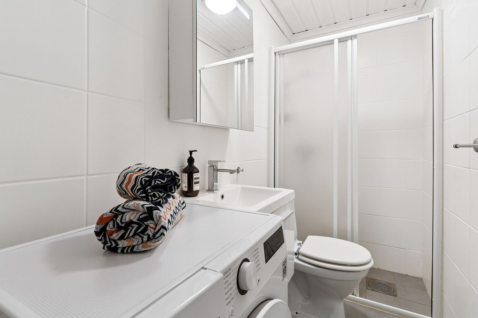 Pent flislagt bad med dusjhjørne og vaskemaskin. Galleribilde