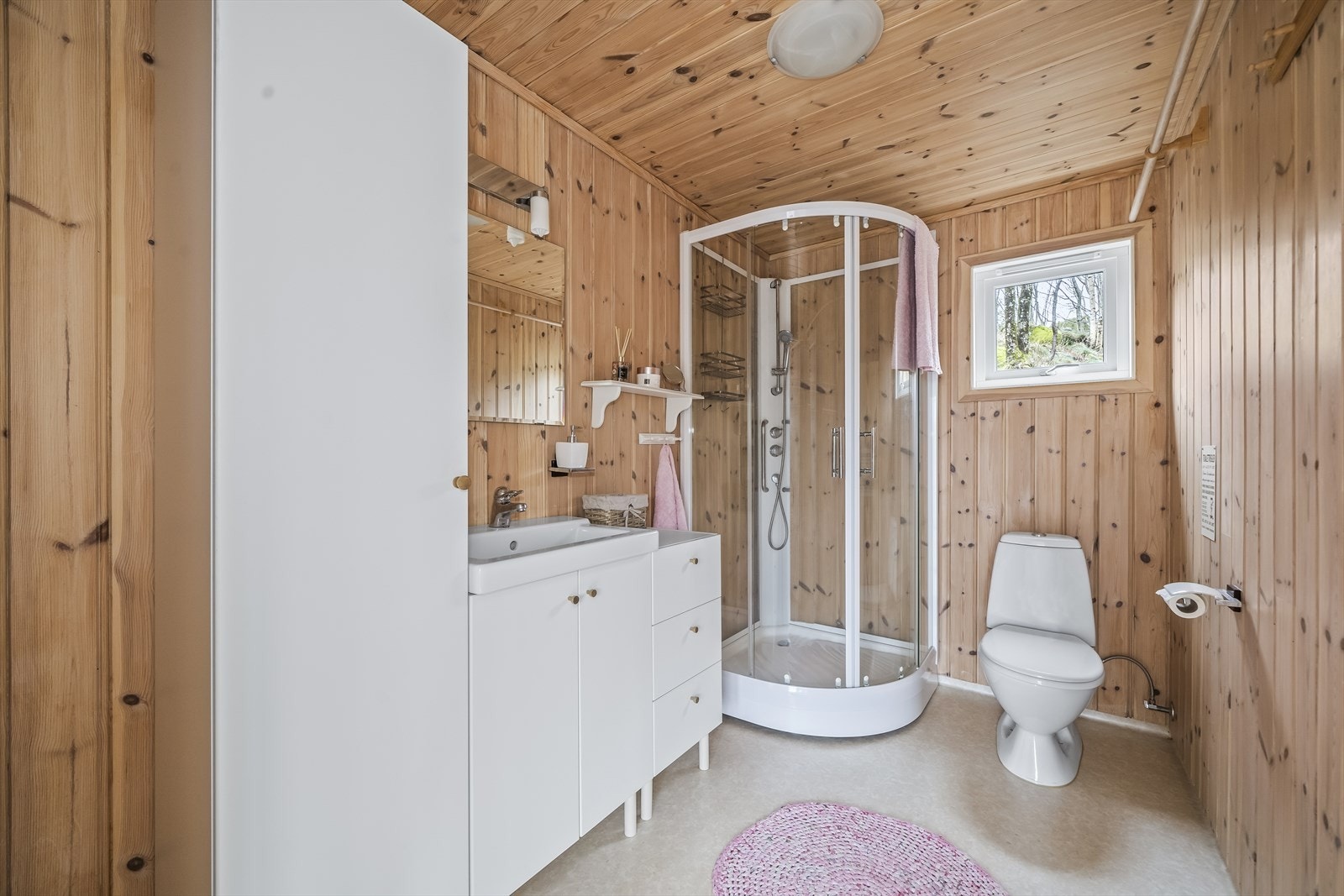 Pent bad med belegg på gulv og panel på vegger. Innredet med baderomsinnredning, toalett og dusjkabinett. Galleribilde