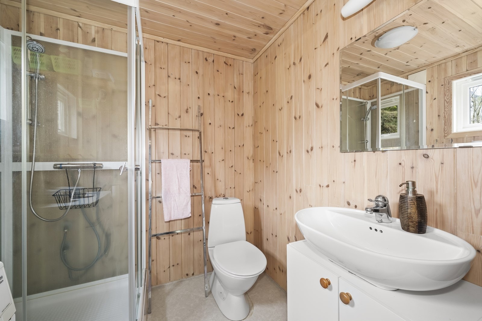 Bad med belegg på gulv og panel på vegger. Innredet med baderomsinnredning, toalett og dusjkabinett. Galleribilde