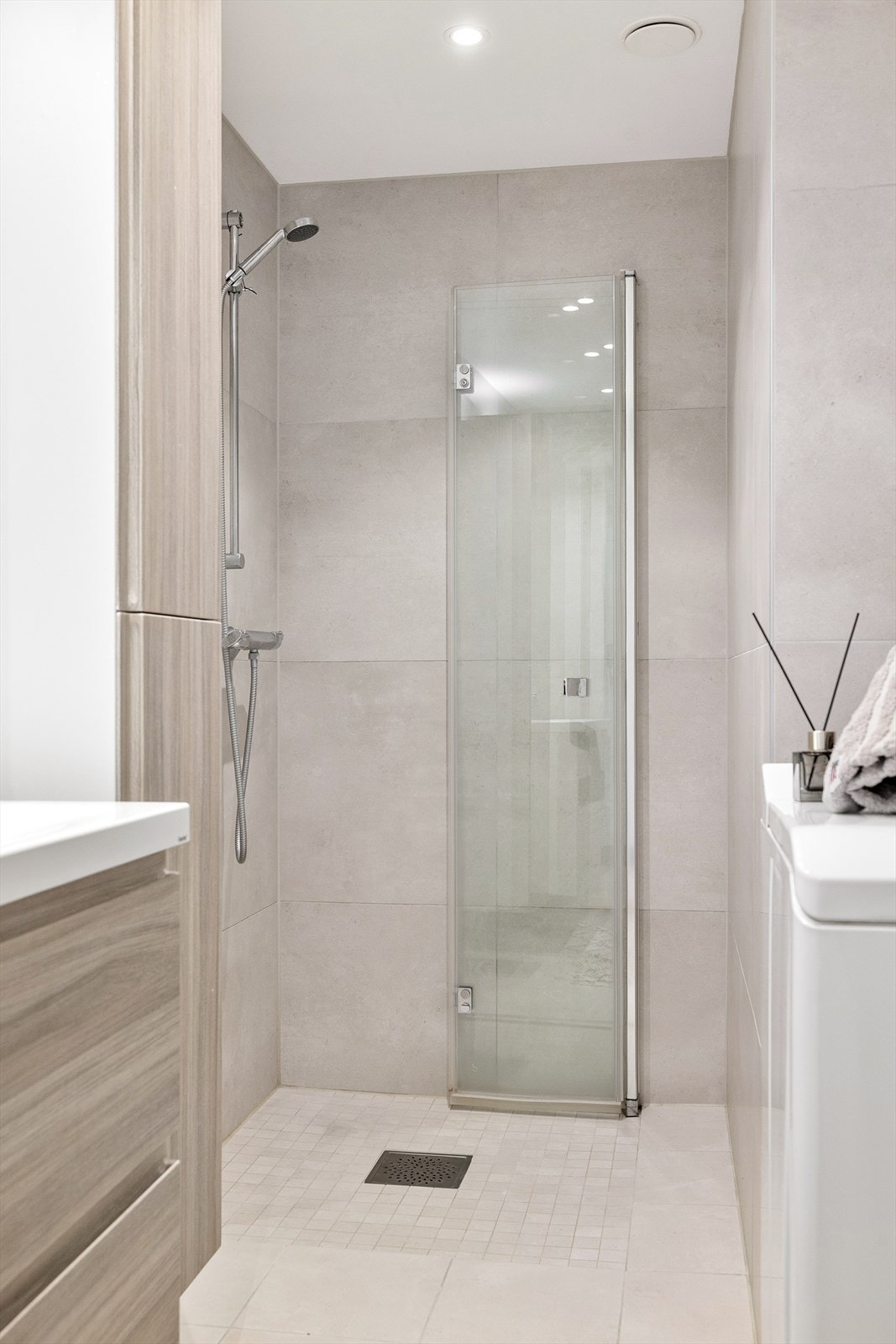 Badet inneholder dusjhjørne med innfellbare dører i glass og baderomsinnredning med skuffer, servant med ett-greps blandebatteri, speilskap på vegg og veggskap. Det er opplegg for vaskemaskin. Galleribilde