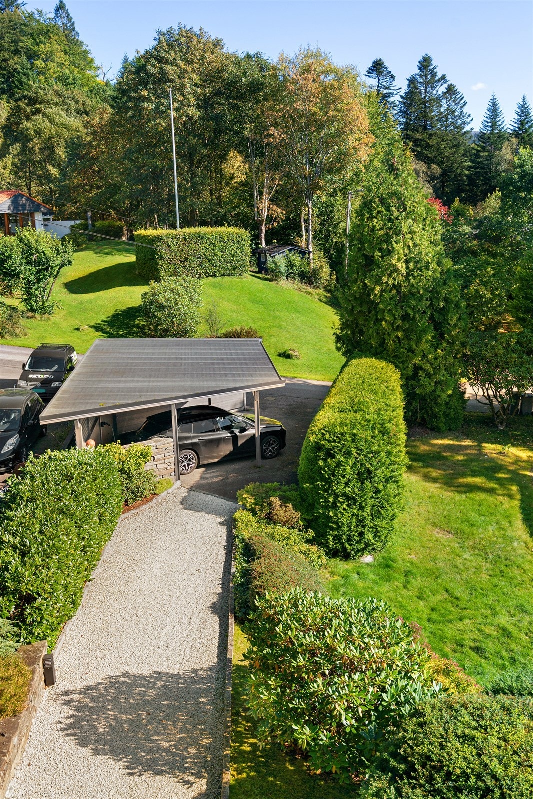 En idyllisk inngangsportal fra bil til hus. Carport med ladestasjon (montert i 2024) og asfaltert grunn. Galleribilde