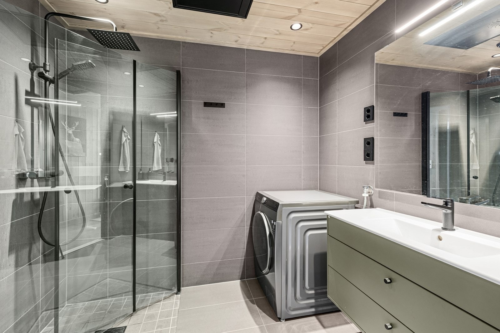 Badet er utstyrt med servant med underskap, speil med tilhørende belysning, dusjvegger, vegghengt wc, og opplegg for vaskemaskin. Galleribilde