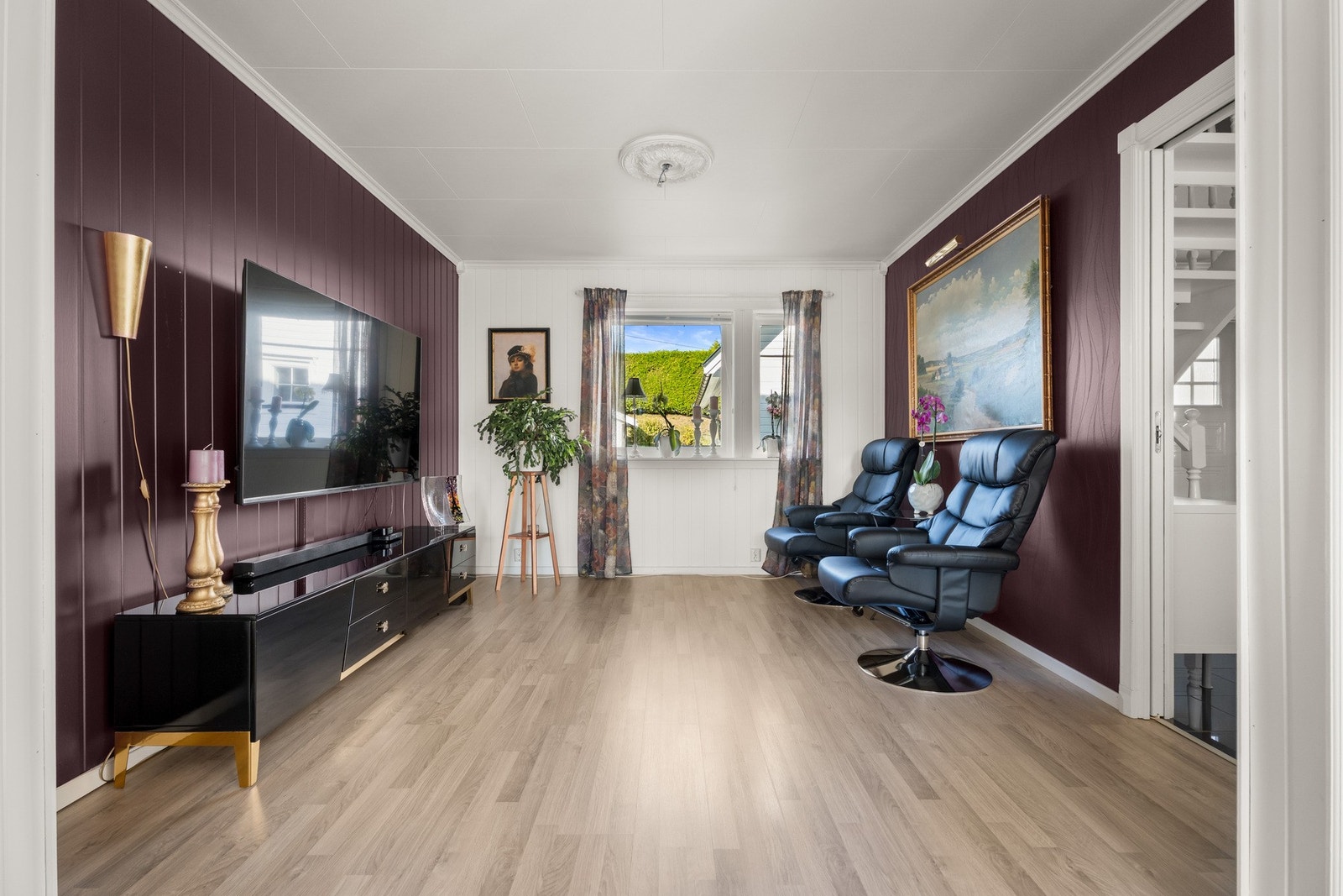 I en egen del kan det innredes med godstoler og tv-møblement, og her er veggene malt i en dyp lillatone som står godt til laminatgulvet Galleribilde